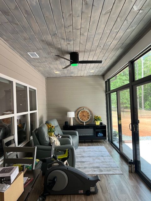 Sunroom with gray ceiling, glass doors, green armchair, rug, clock, and a stationary bike.