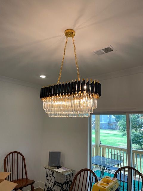 Gold and black crystal chandelier hanging in a room, with a window and chairs visible.