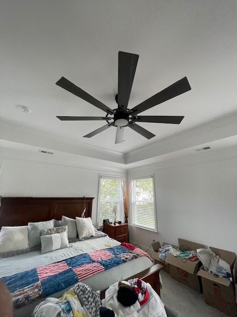 Bedroom with a dark ceiling fan, bed with blue quilt, white walls and windows.