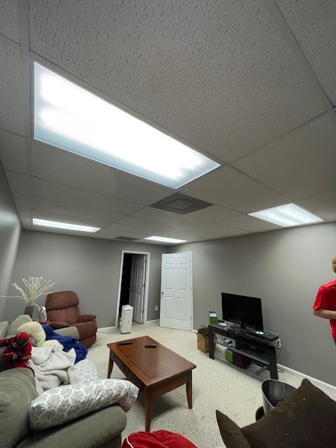A basement room with a TV, sofa, coffee table, and fluorescent lights. Gray walls, white ceiling.