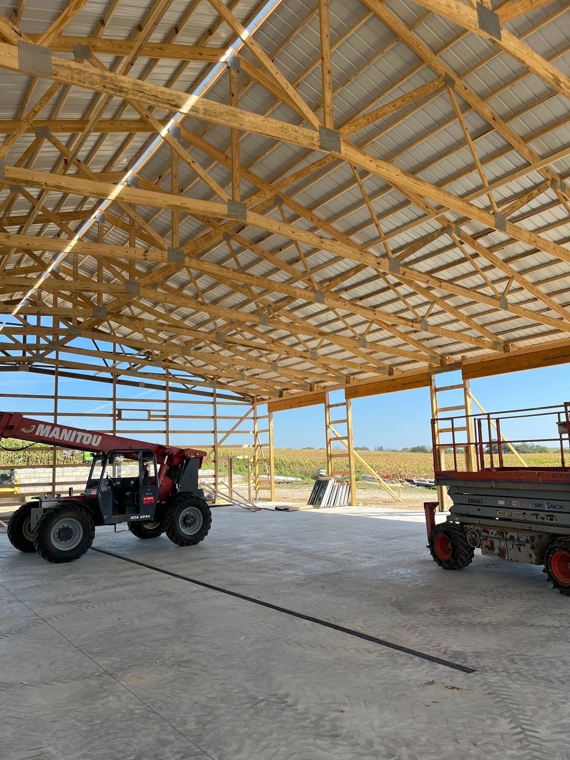 A tractor and a scissor lift are parked inside of a building under construction.