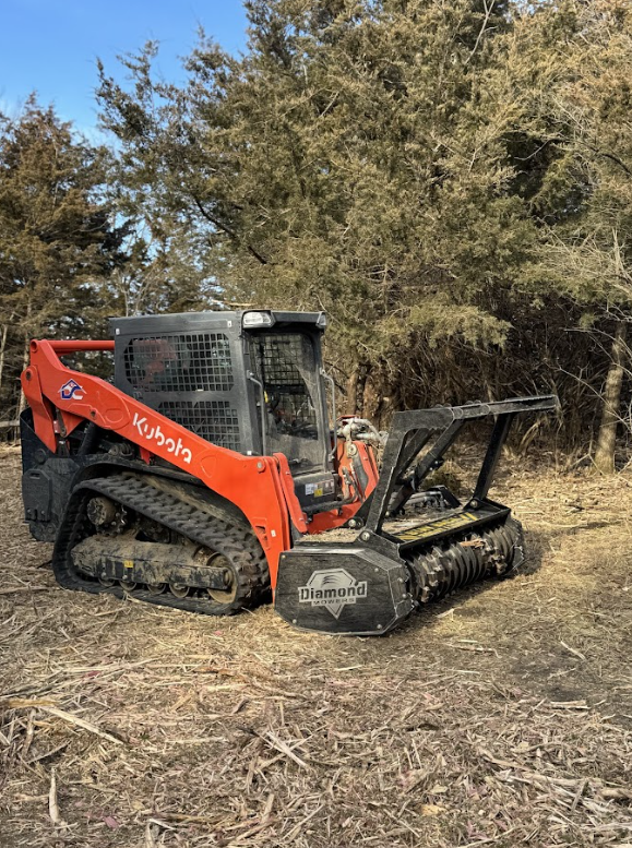 A red and black tractor is driving through a forest.