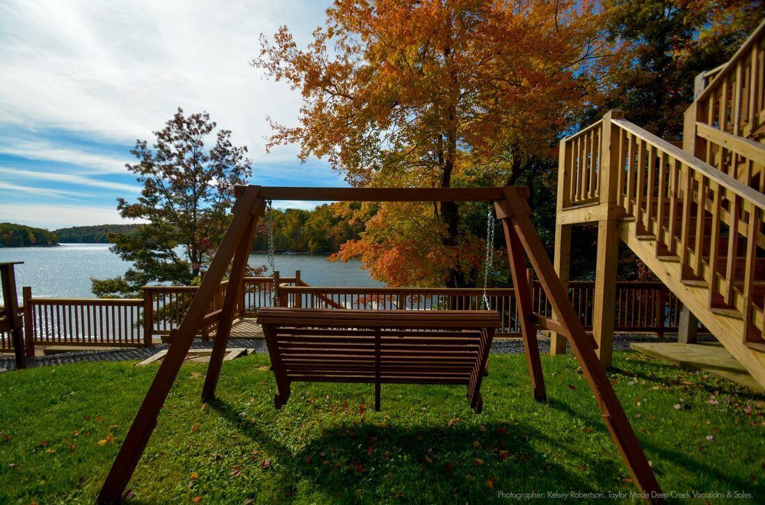 A wooden swing is sitting in the grass near a lake.