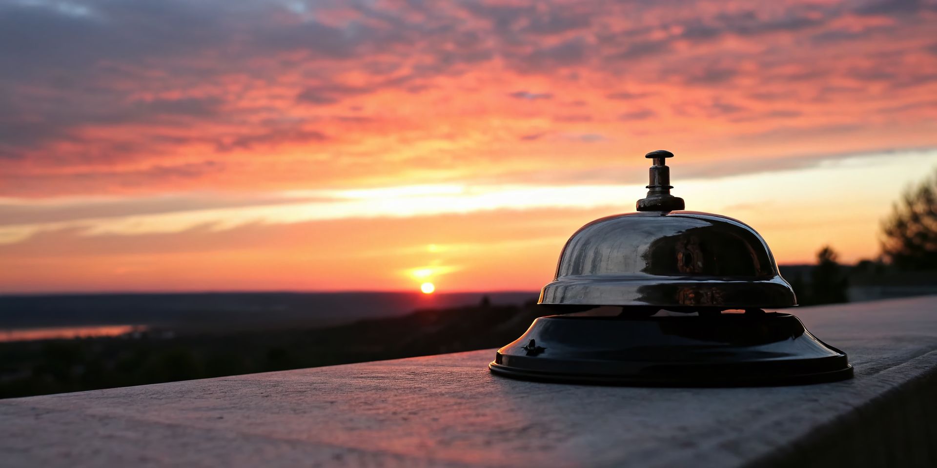 A bell is sitting on a ledge with a sunset in the background.