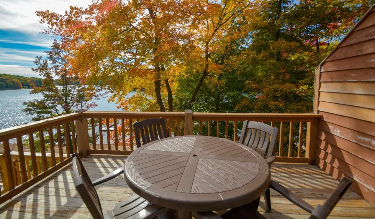 A wooden deck with a table and chairs overlooking a lake.
