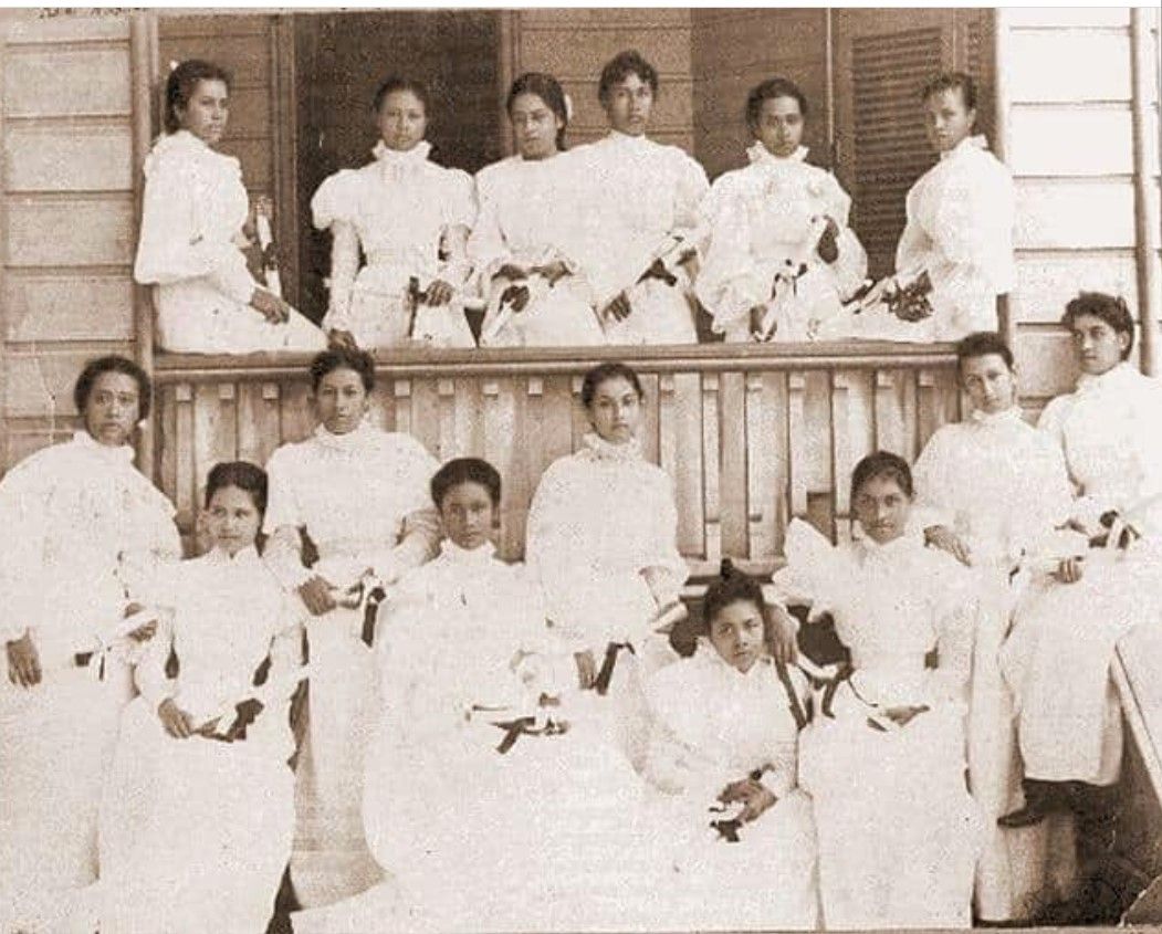 Group of women in white dresses posing on a balcony.