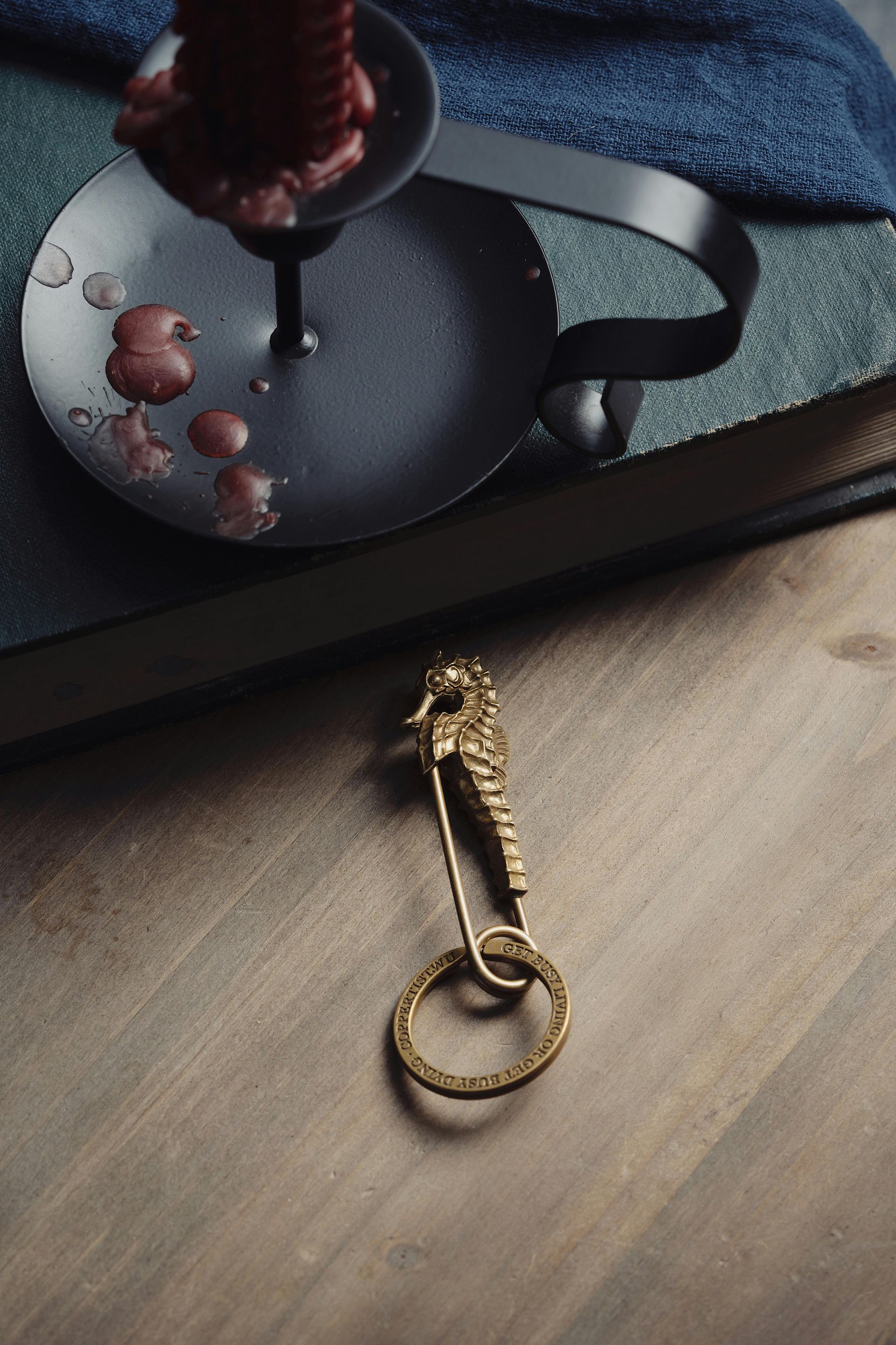 A vintage key chain with a seahorse charm sits on a wooden table next to a candle holder and book.
