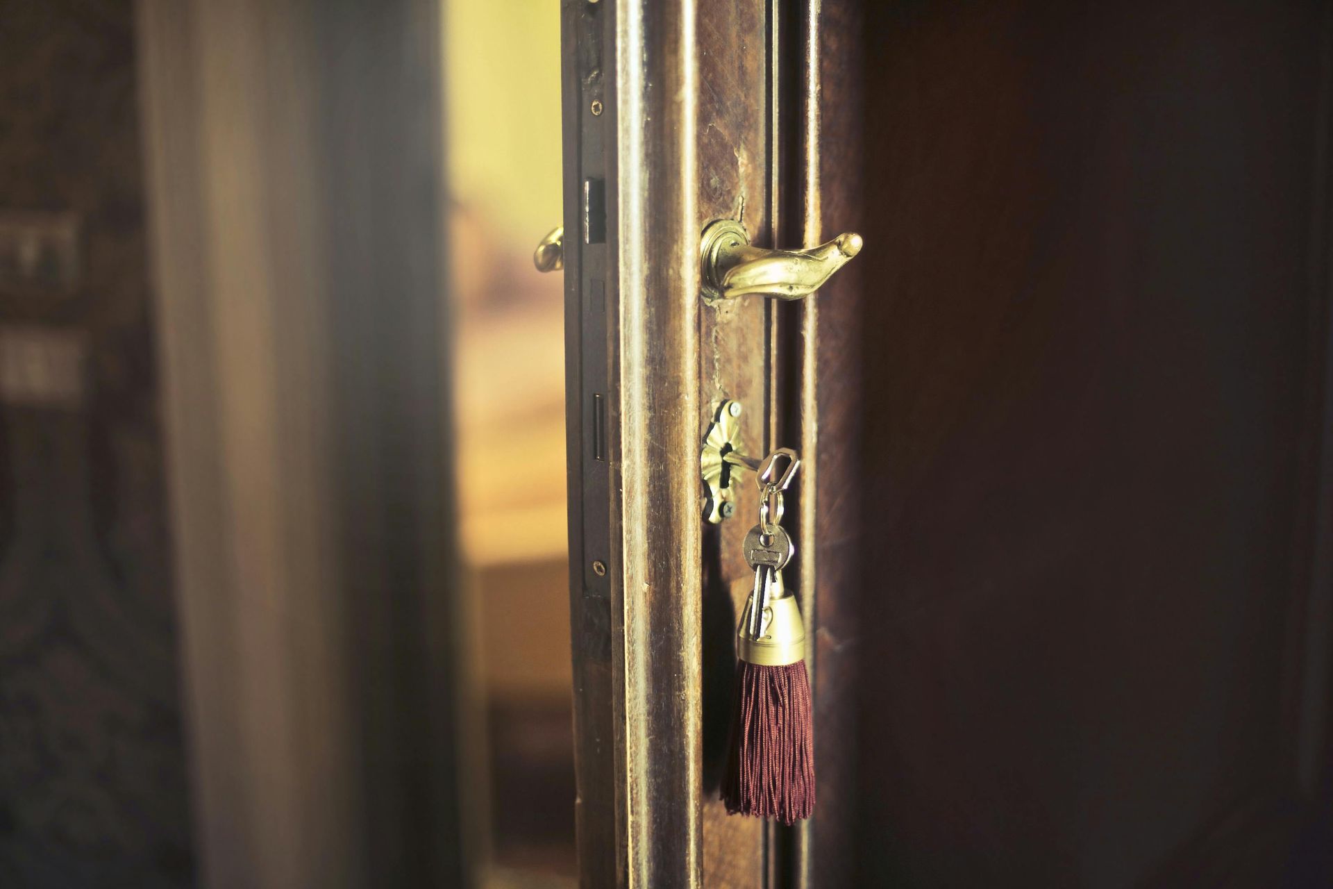 Close-up of a wooden door with a golden handle, key in the lock with red tassel.