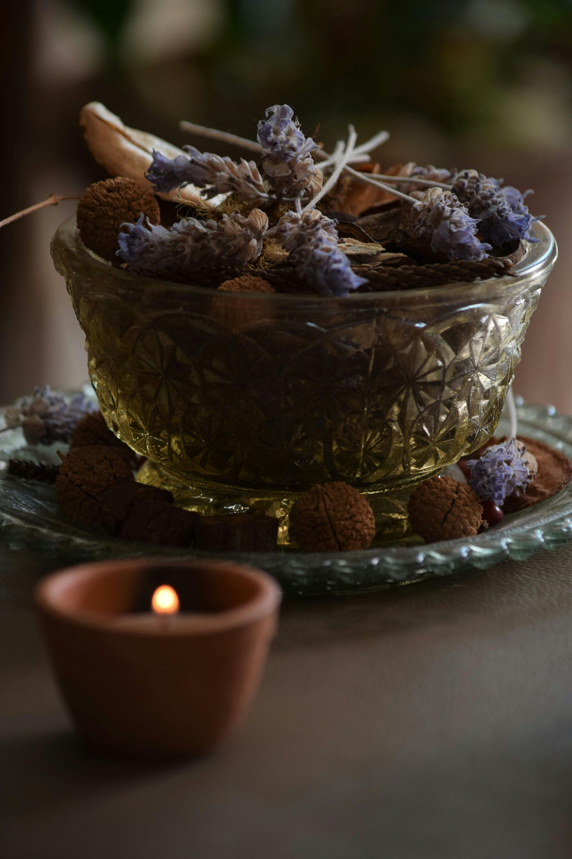 Bowl of dried lavender, potpourri, with a lit candle in the foreground. Soft lighting.