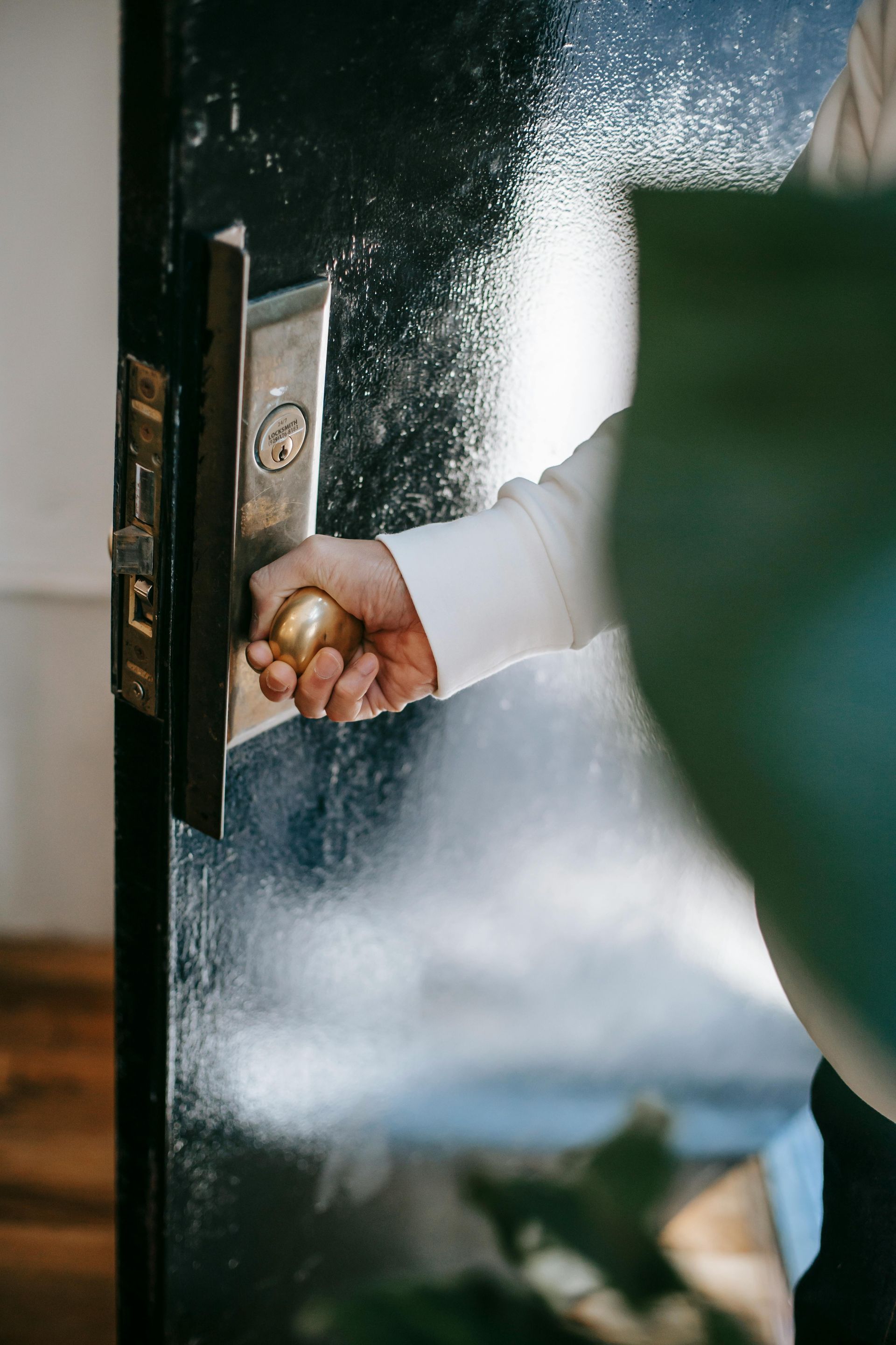 Person's hand opening a black door with a gold doorknob. Sprayed mist in the air, close-up.
