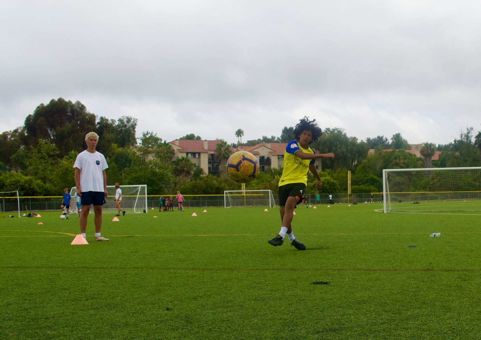 Children practicing soccer on a grassy field with cones and goals in the background