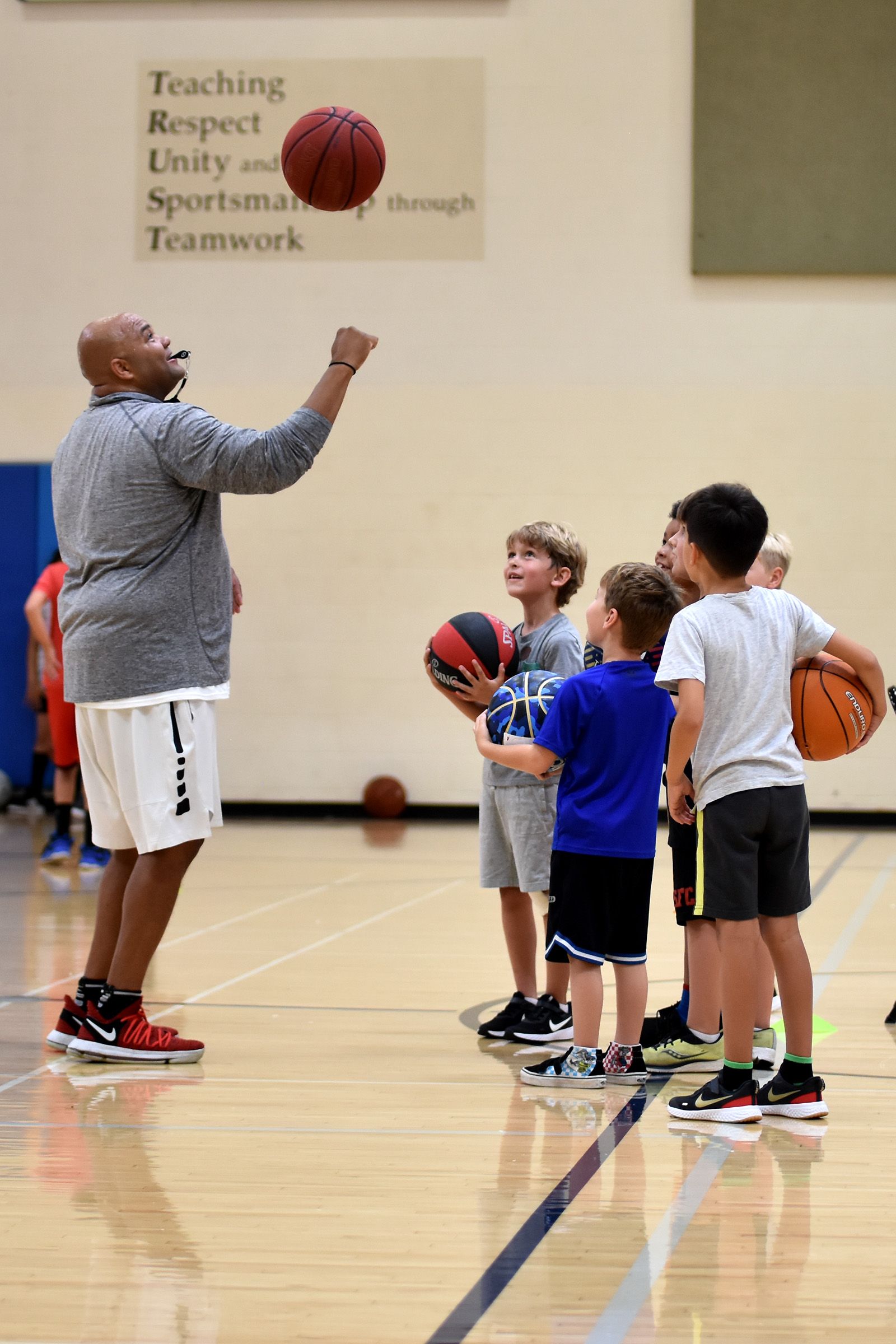 Basketball coach instructing children in a gym, with kids holding basketballs during practice