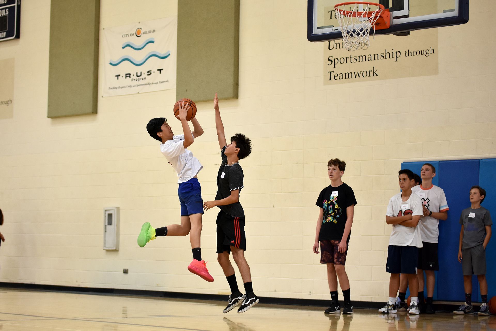 Basketball player jumping for a shot in a gym while others watch from the sideline
