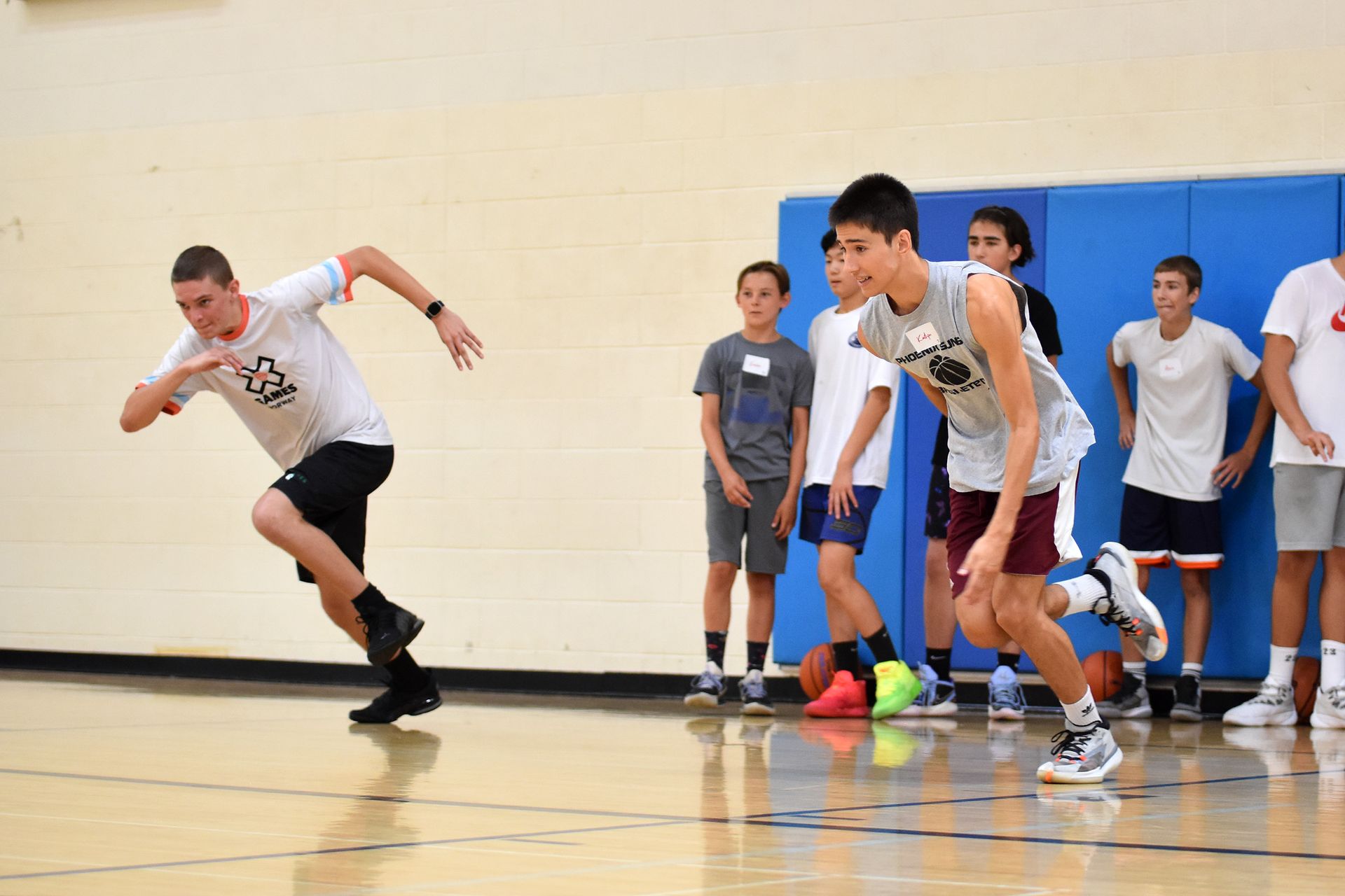 Students sprinting in a gym during a drill, with others watching from the sideline.