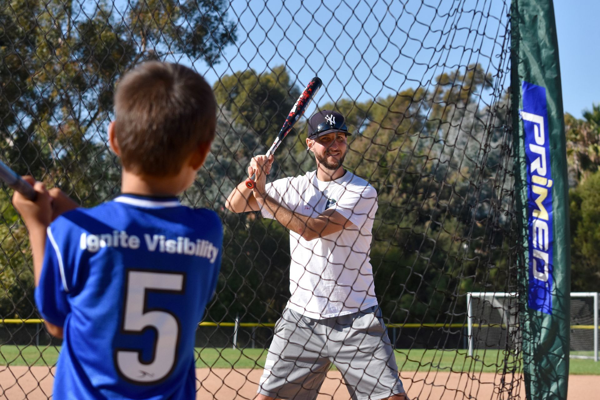 Baseball coach instructing a child batter at batting practice behind a net