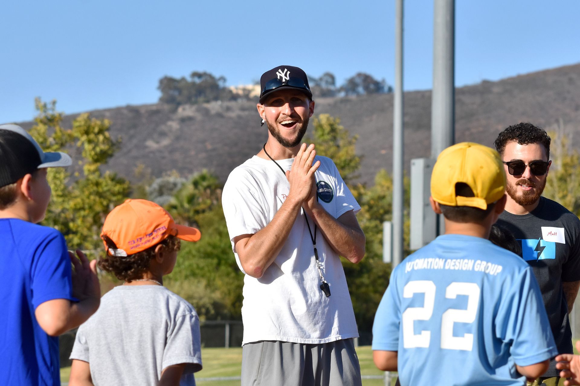 Coach speaking to a group of children outdoors on a sunny field.