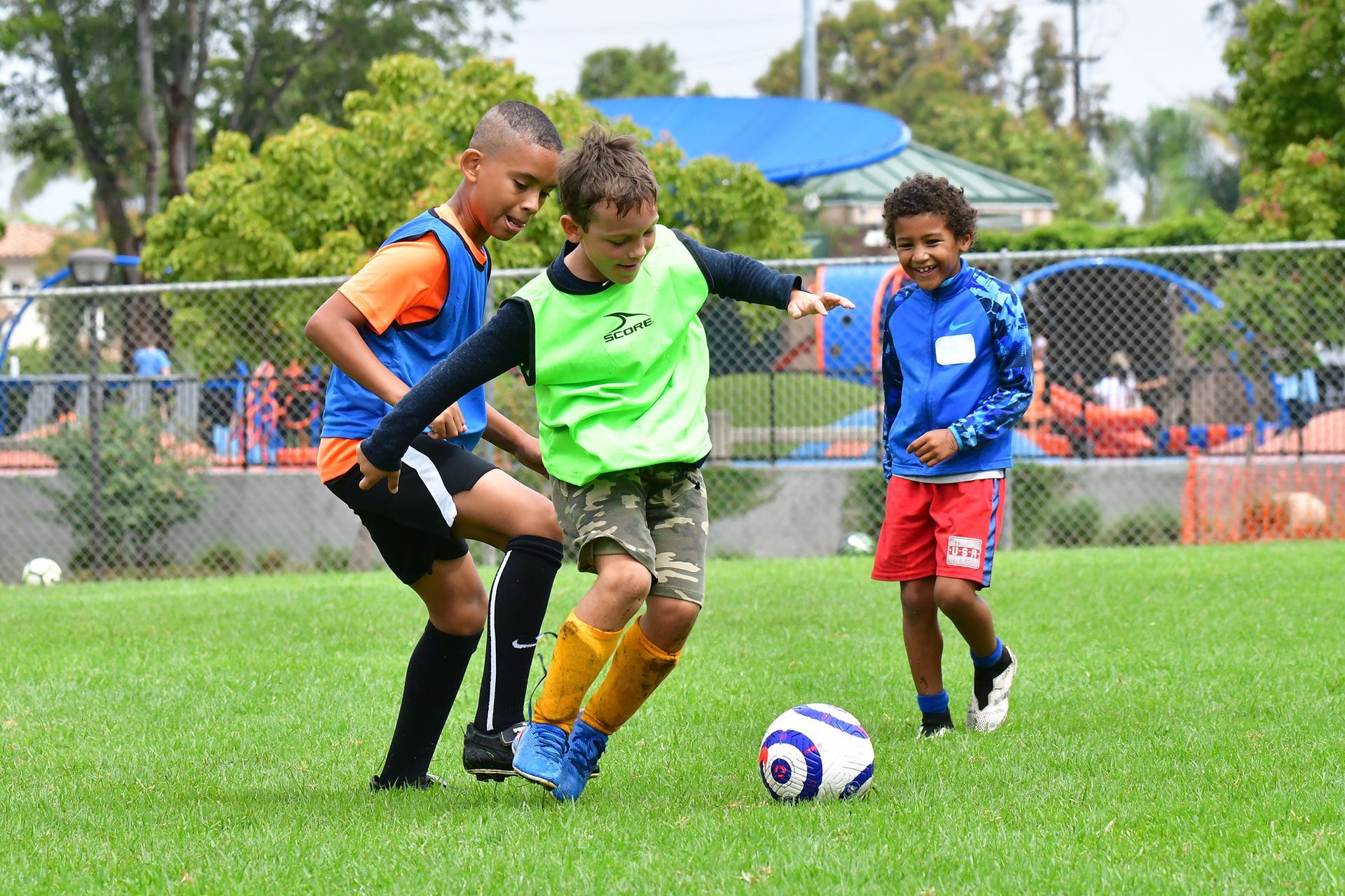 Two children and an adult playing soccer on a grassy field, chasing a blue-and-white ball
