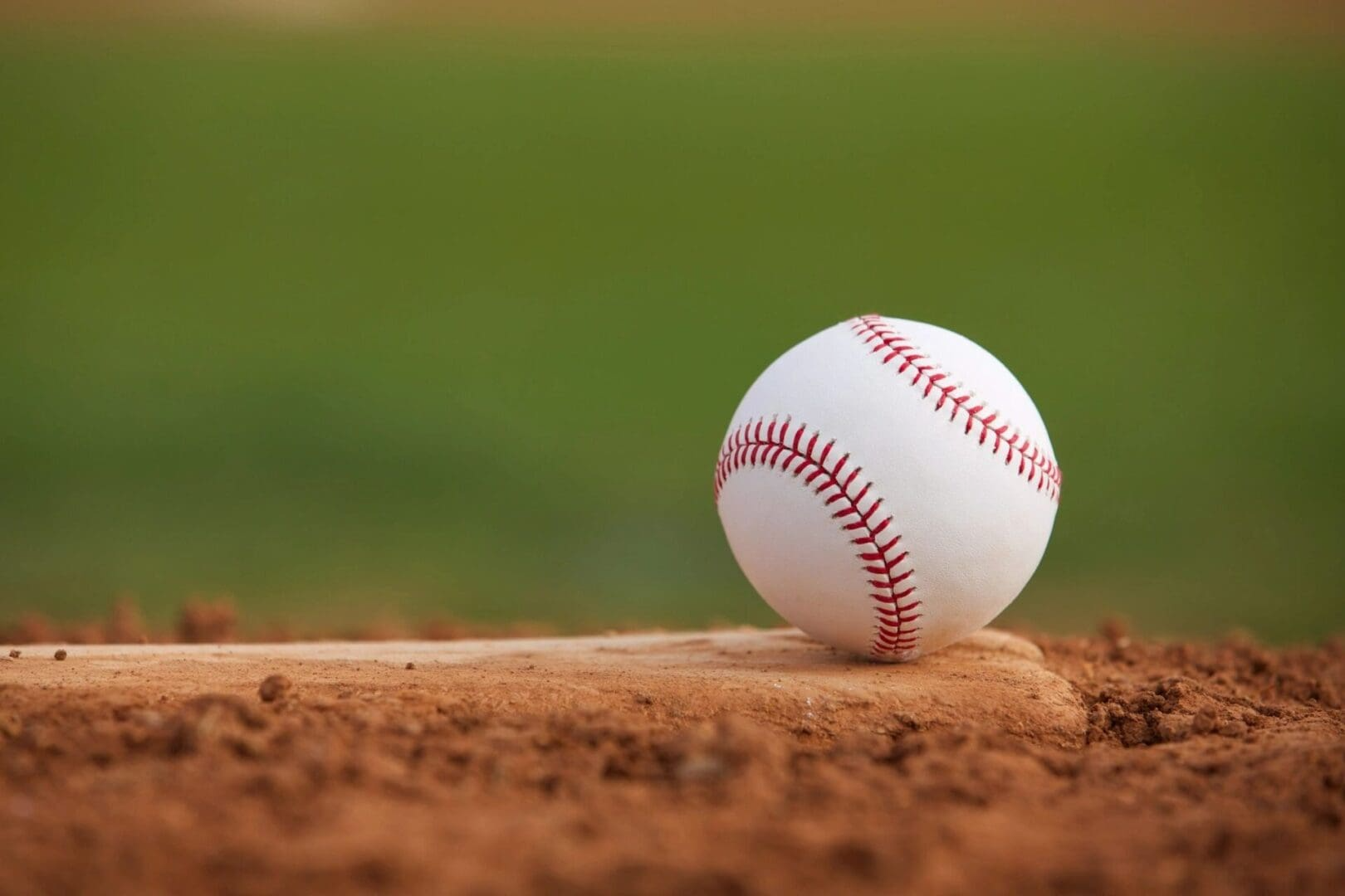 Baseball resting on a dirt field with a blurred green background