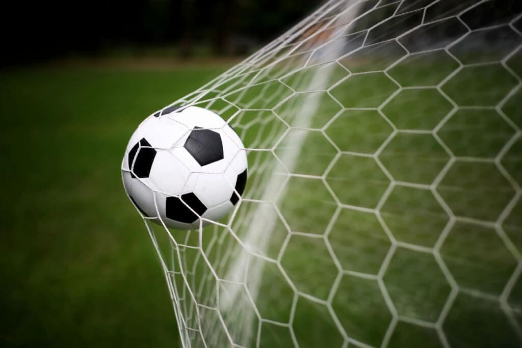 Soccer ball hitting the net on a goal, with a green field blurred in the background