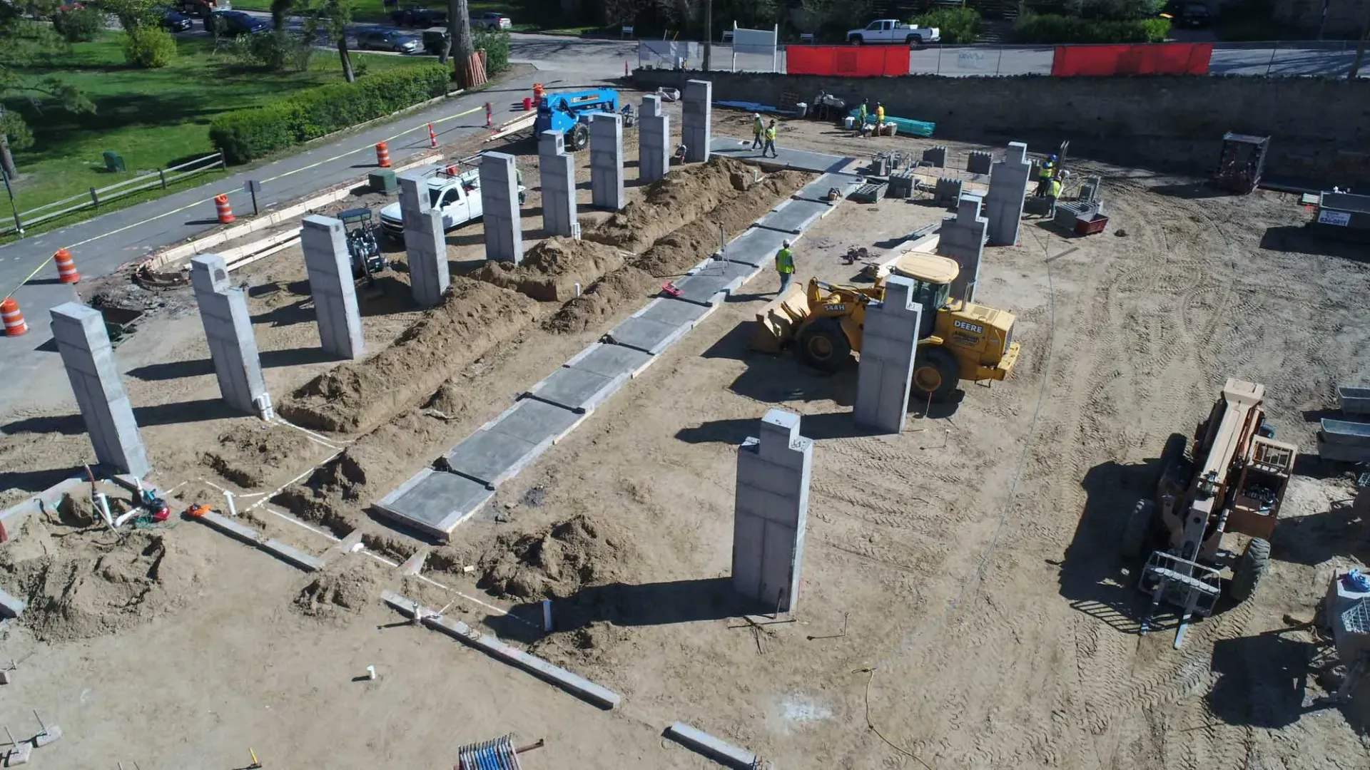 Construction worker measures a concrete pillar at a construction site; wearing a yellow hard hat and vest.