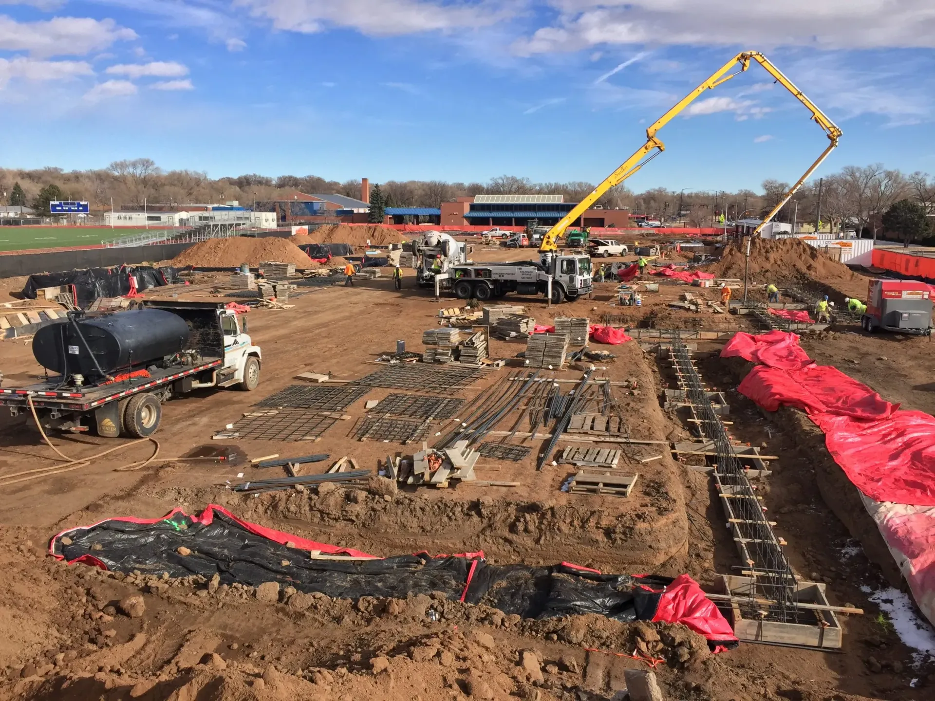 Construction site with concrete foundations and support structures, trees in the background.