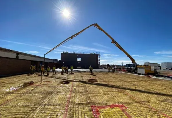 Construction workers on a site laying asphalt, wearing safety vests and helmets.