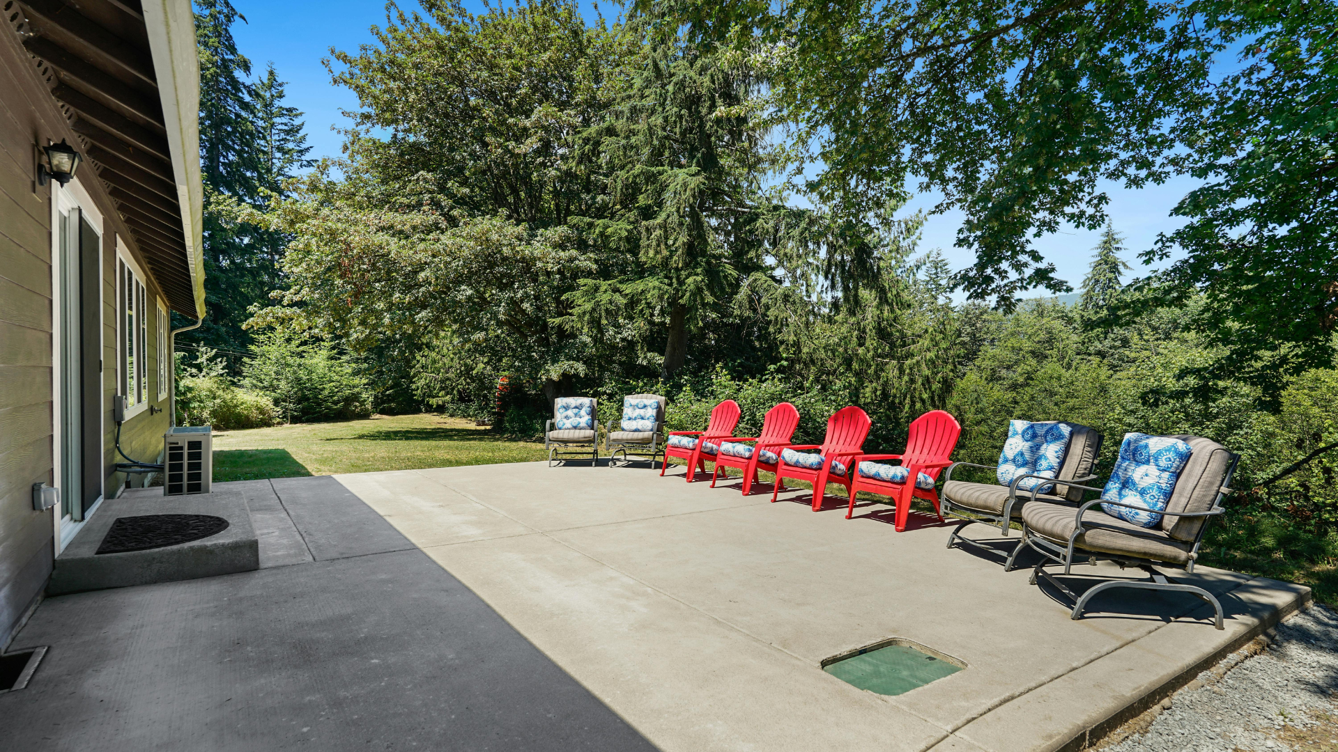 White walled patio with built-in wooden bench, gray cushions, tree, and black outdoor speakers.