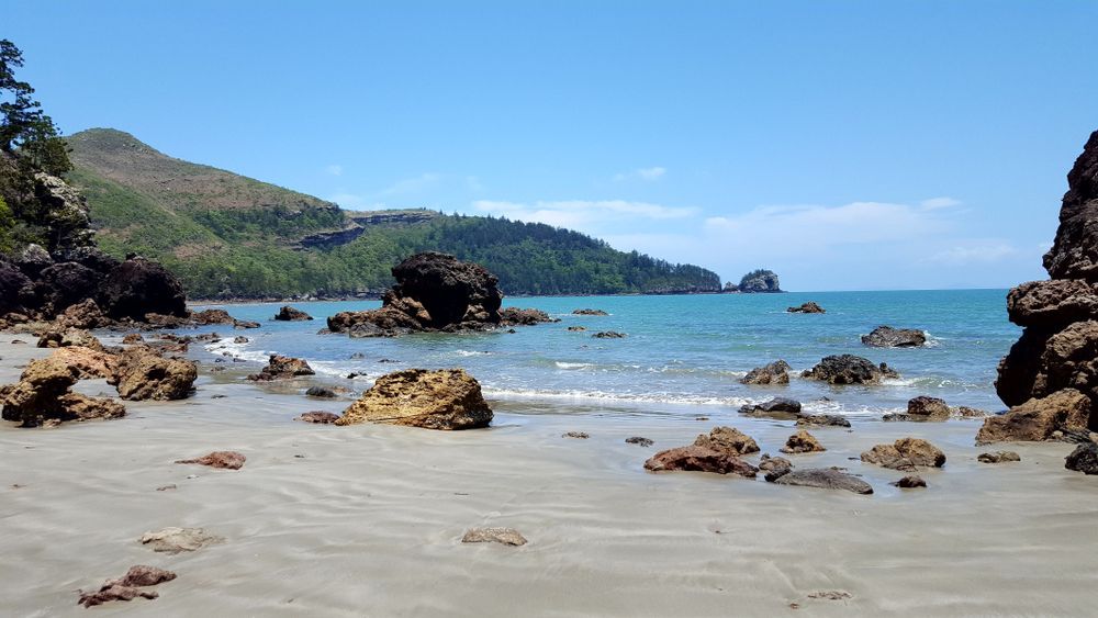 A Beach With Rocks In The Water And Mountains In The Background — Custom Steel Fab in Mackay, QLD