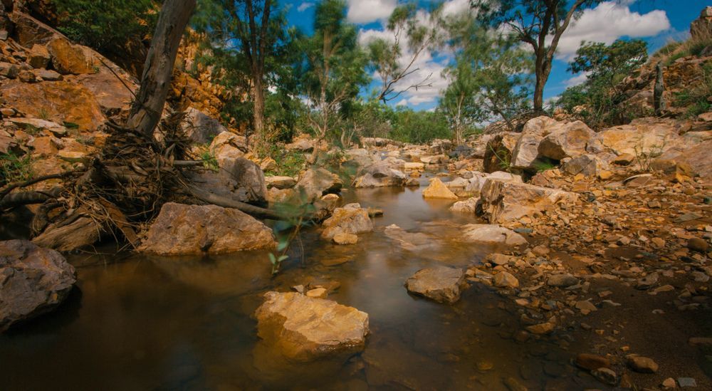 A Stream Running Through A Rocky Area Surrounded By Trees And Rocks — Custom Steel Fab in Mount Isa, QLD