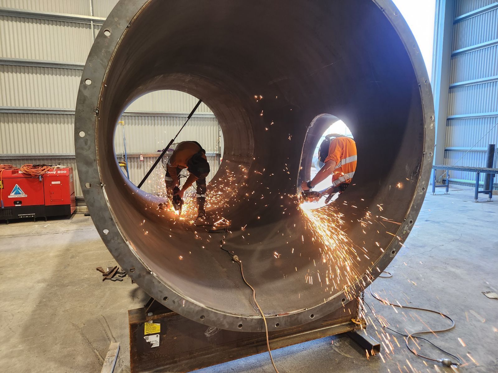 A man is cutting a large metal pipe in a factory.