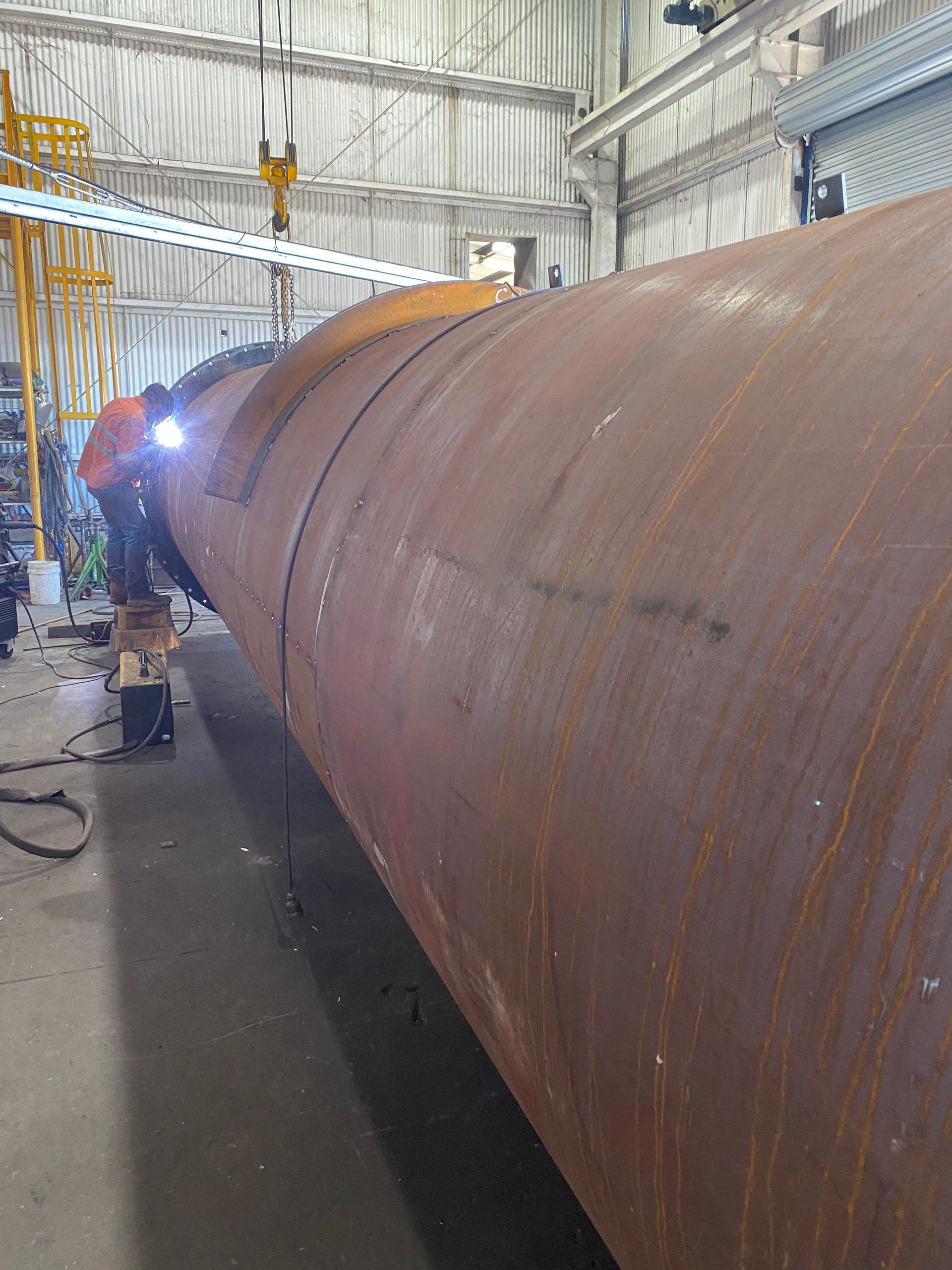 A Man Is Welding A Large Rusty Pipe In A Factory — Custom Steel Fab in Garbutt, QLD