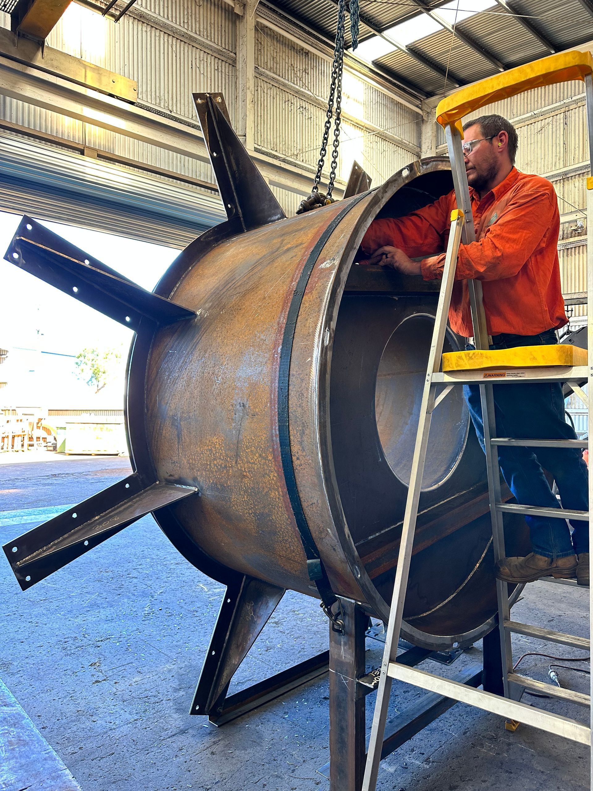 A man is standing on a ladder next to a large metal object.