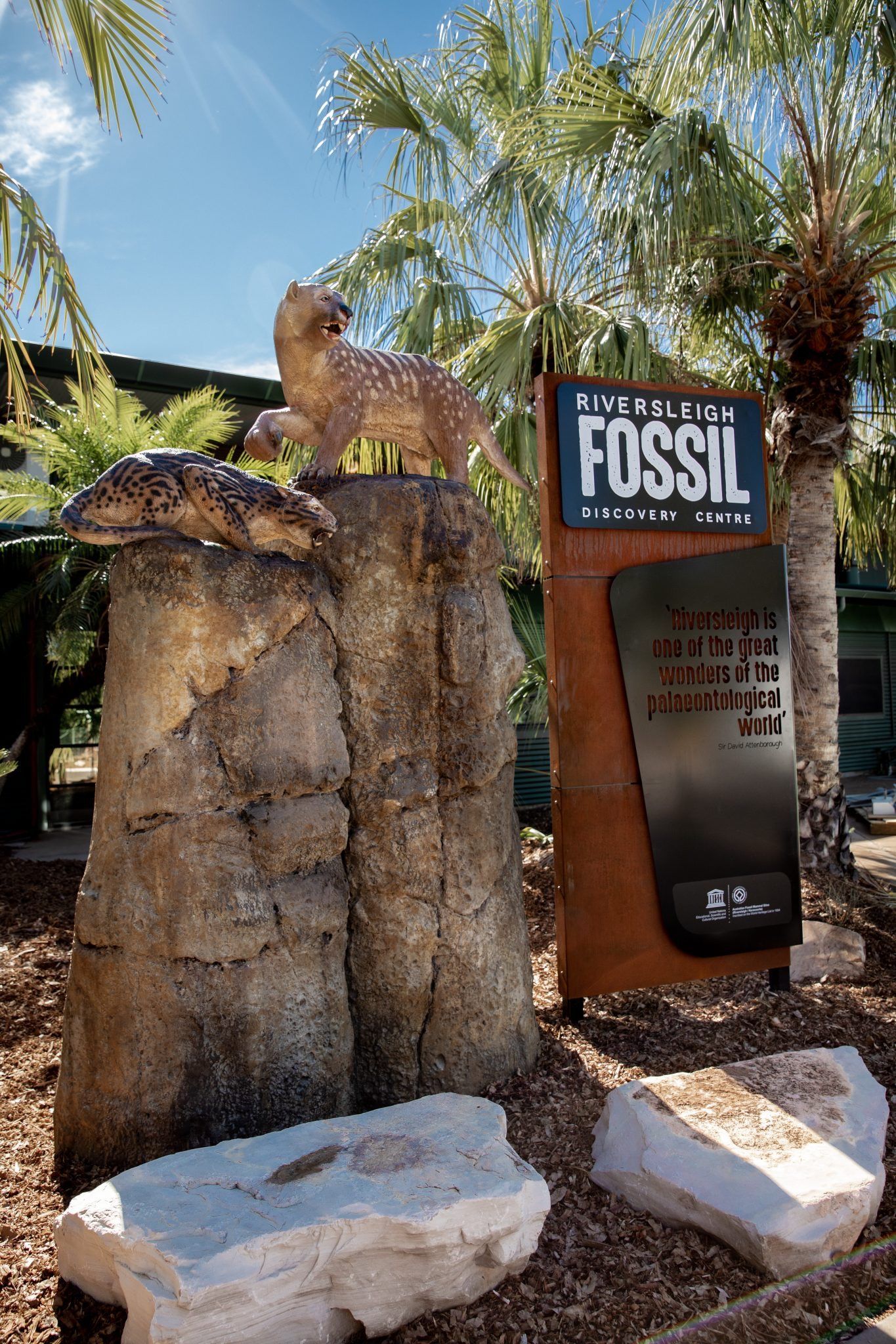 A statue of a lizard is sitting on top of a rock next to a sign that says fossil.