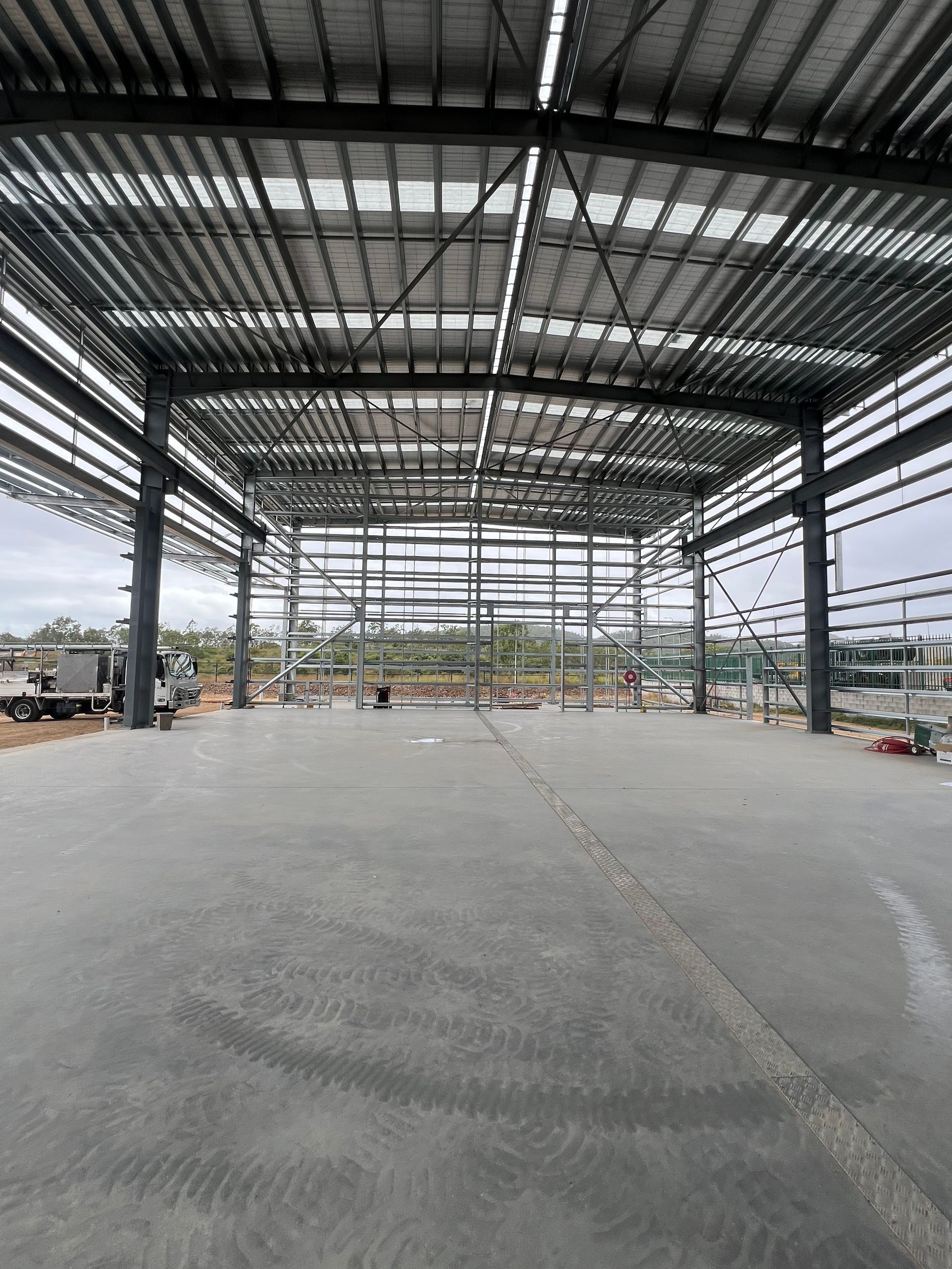 A Large Warehouse Under Construction With A Concrete Floor And A Metal Roof — Custom Steel Fab in Garbutt, QLD