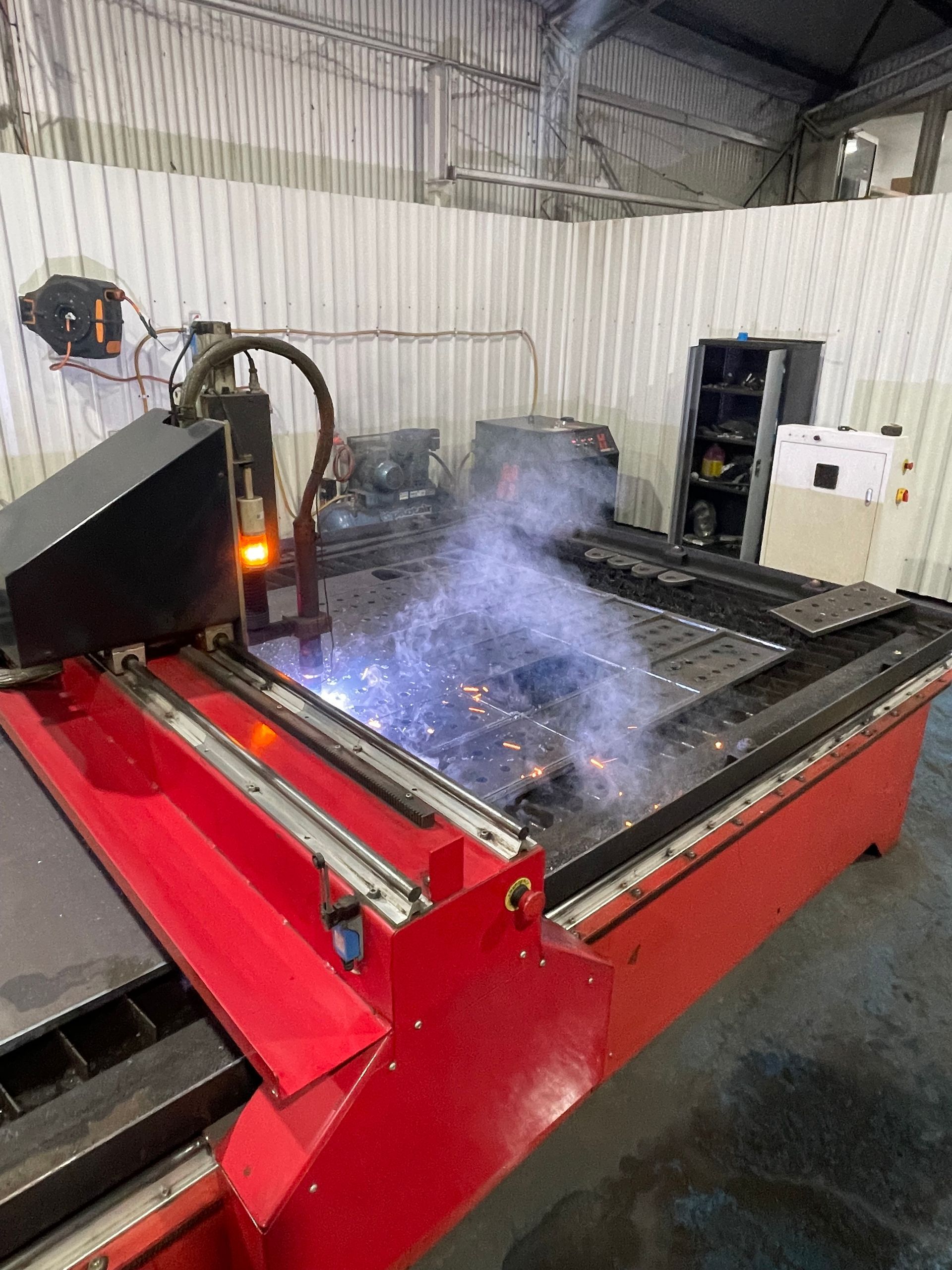 A red machine is cutting a piece of metal in a warehouse.