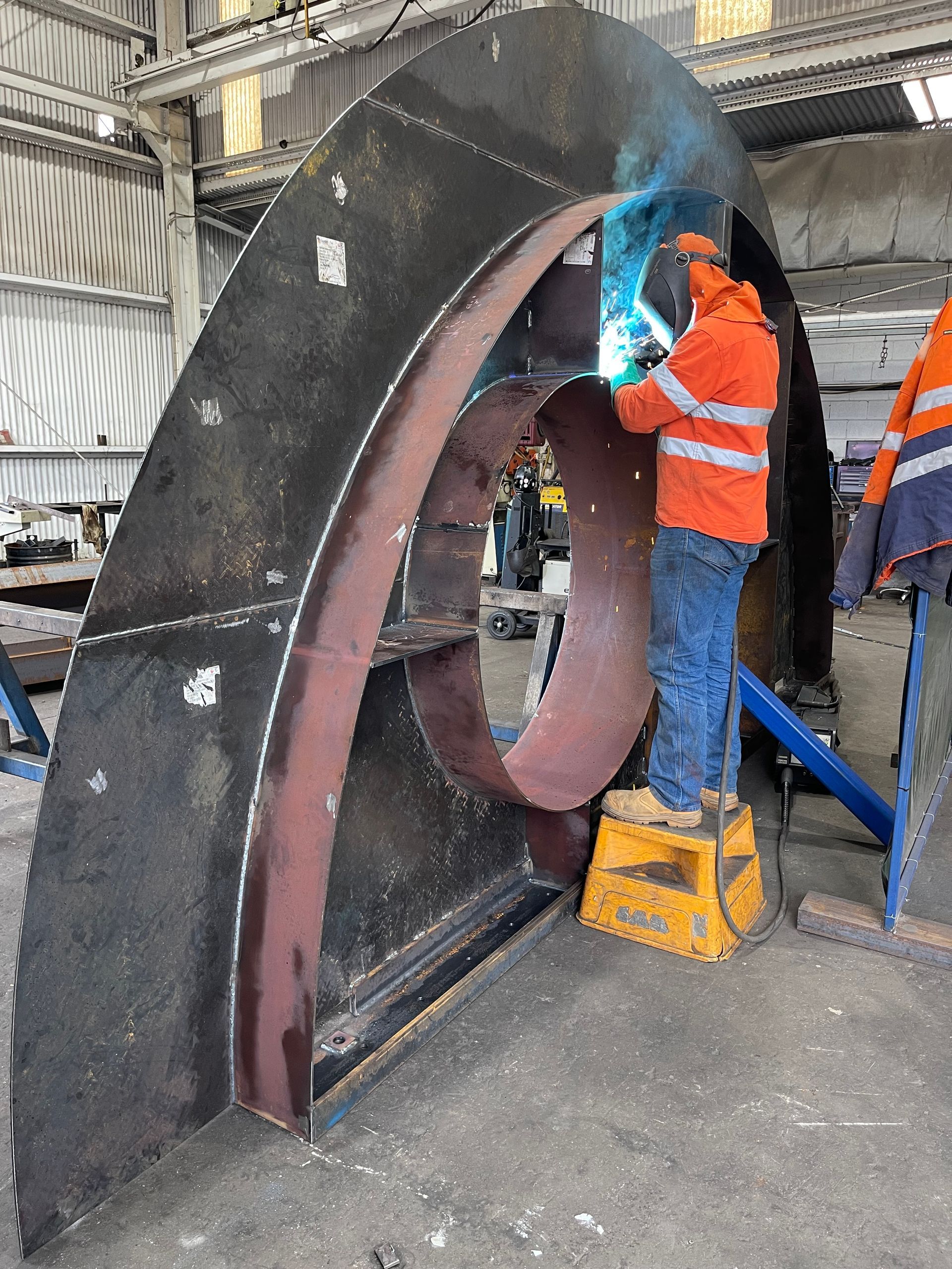 A Man Is Welding A Large Piece Of Metal In A Factory — Custom Steel Fab in Garbutt, QLD