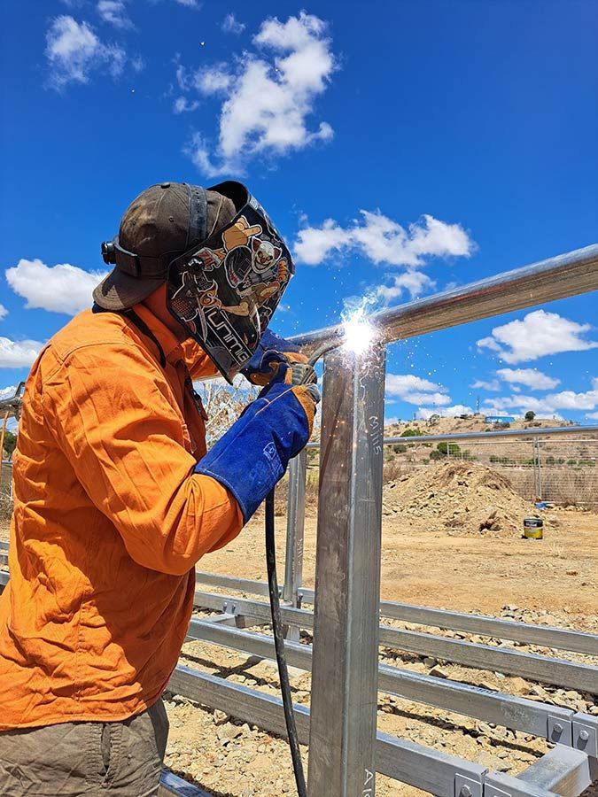 A Man Wearing A Helmet And Gloves Is Welding A Metal Fence — Custom Steel Fab in Alice Springs, NT