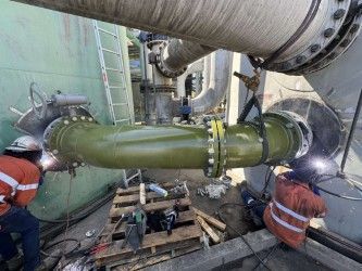 A Man Is Welding A Pipe In A Factory — Custom Steel Fab in Garbutt, QLD