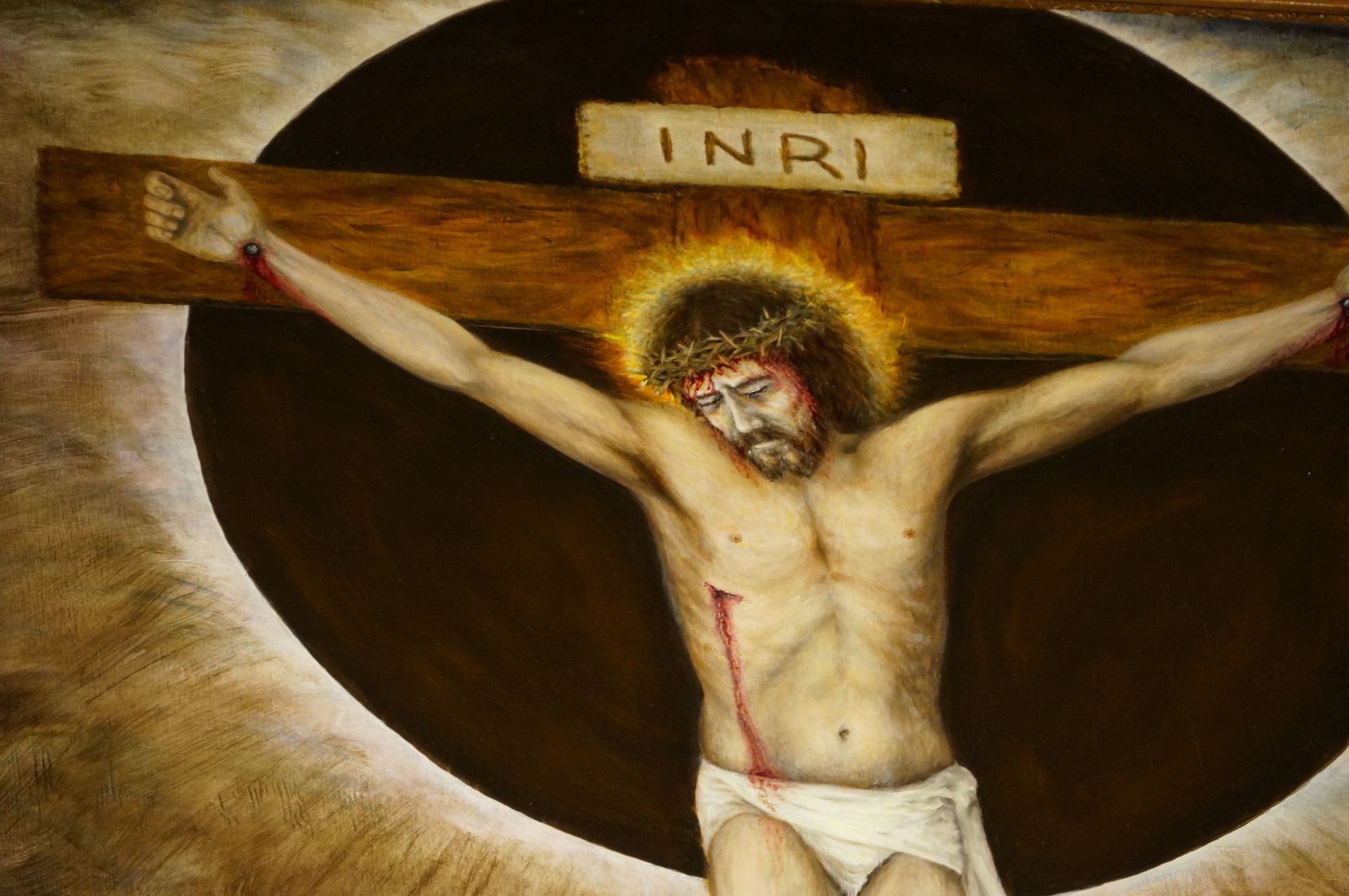 A depiction of the crucifixion of Jesus with a crown of thorns, a halo, and an INRI sign against a dark circular background.