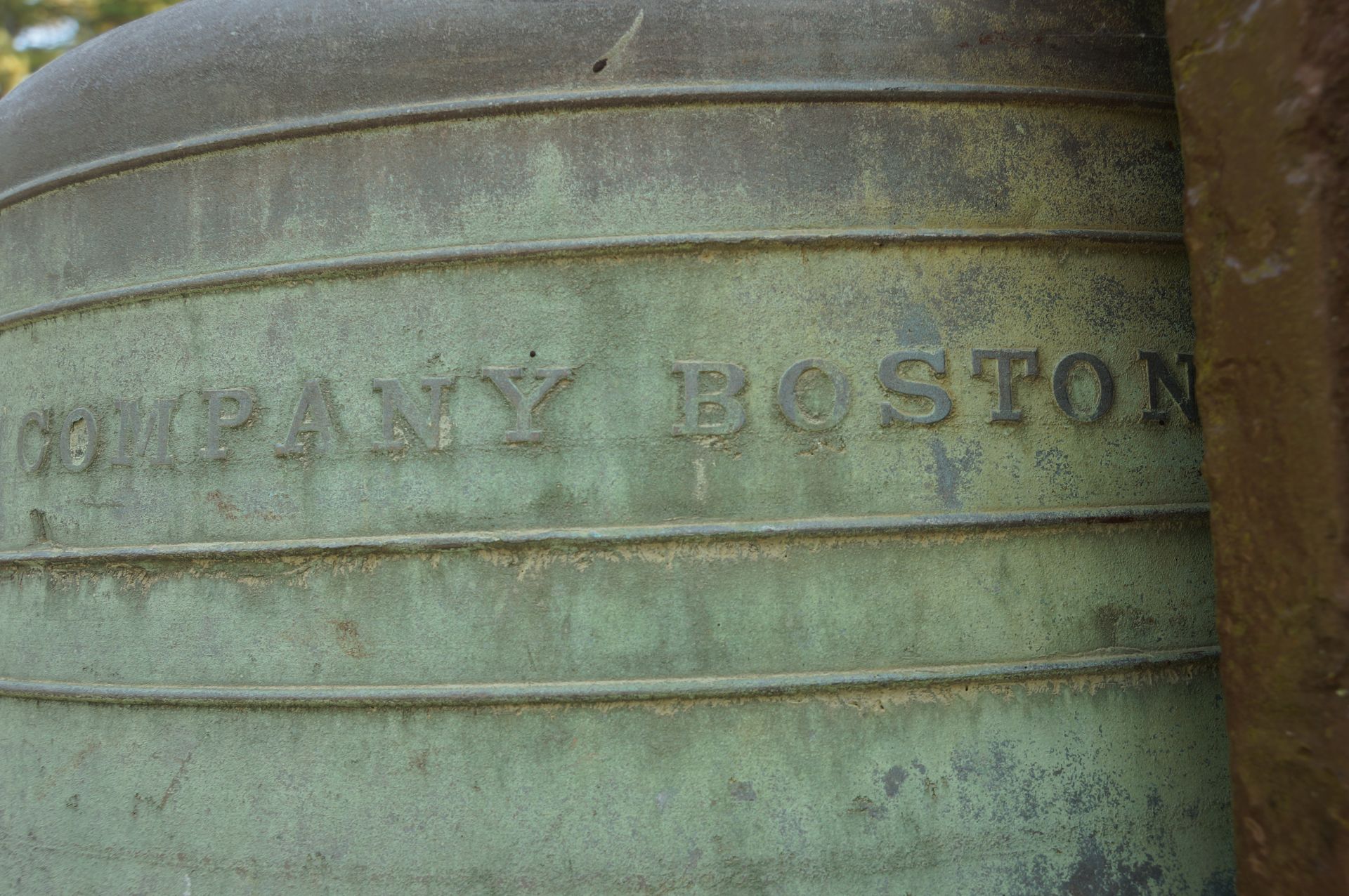 A close-up view of a weathered, green-patina bell with the embossed text 