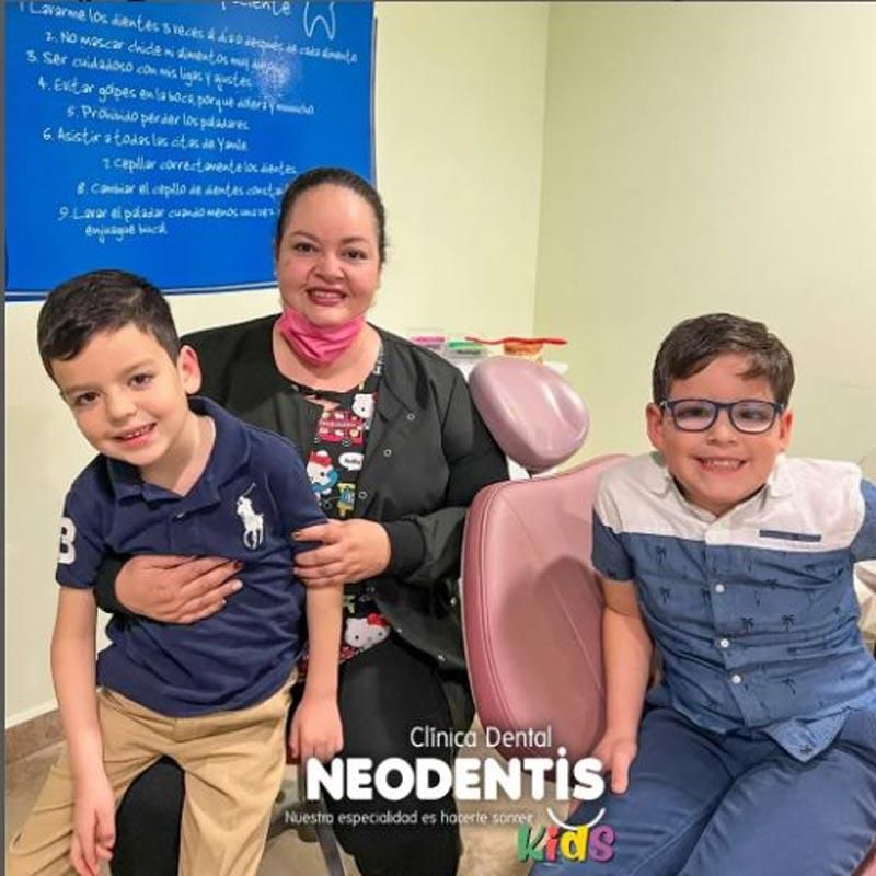 Una mujer y dos niños pequeños están sentados en un sillón dental en neodentistas