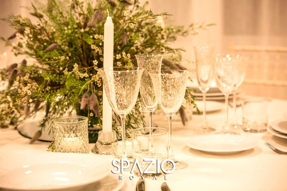 Una tavola apparecchiata con piatti, bicchieri da vino, candele e fiori.