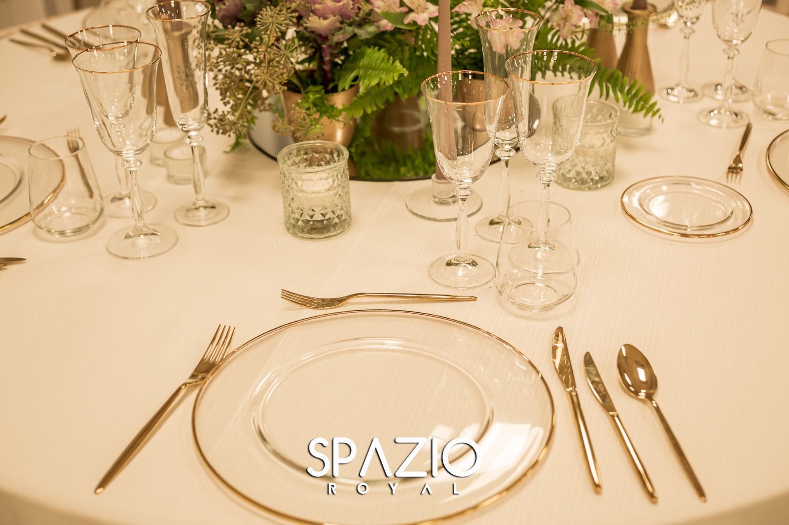 Un tavolo apparecchiato per un ricevimento di nozze con piatti, posate e un vaso di fiori.
