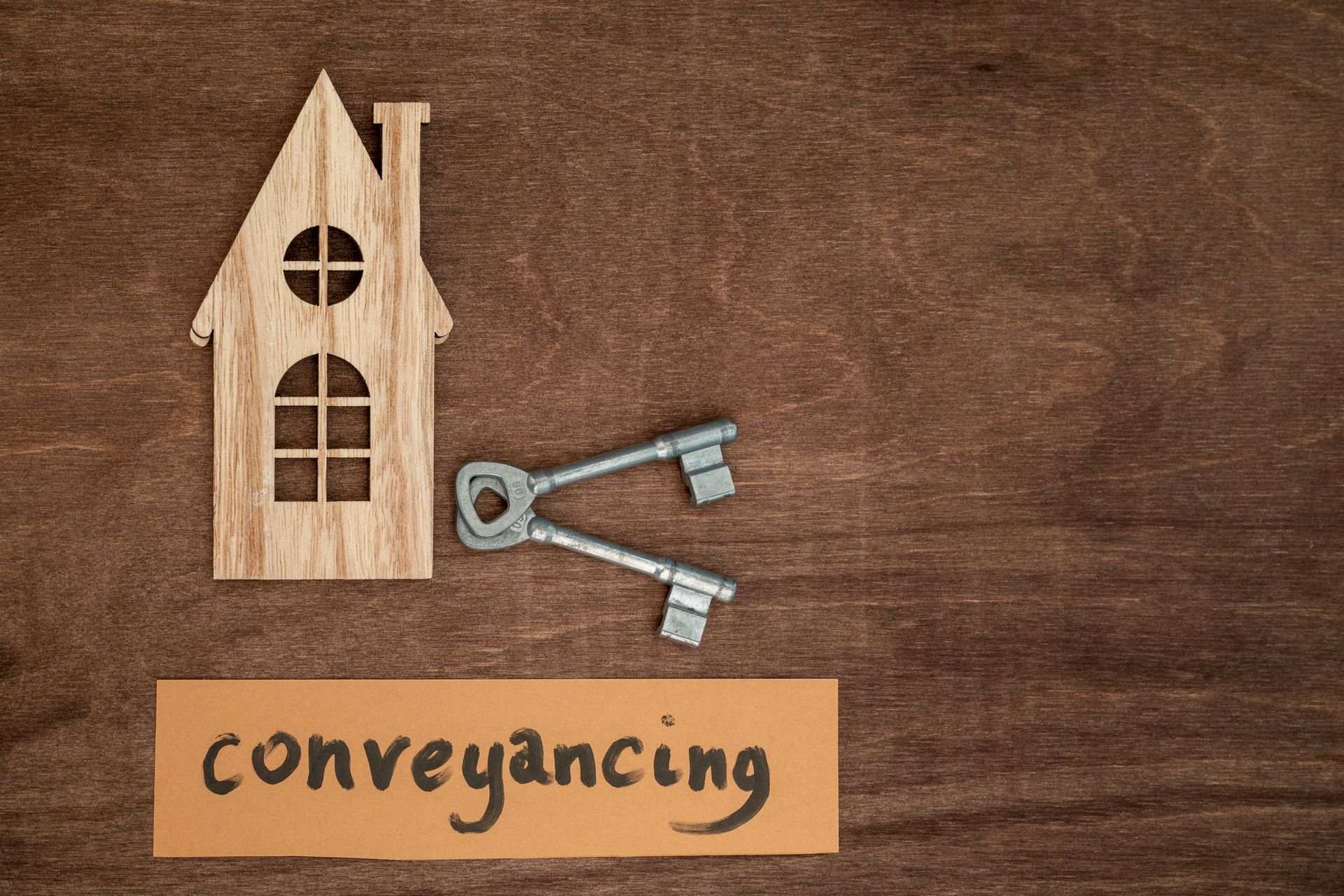 Wooden house model, keys, and “conveyancing” text on wood surface. Wooden house model, keys, and “conveyancing” text on wood surface.