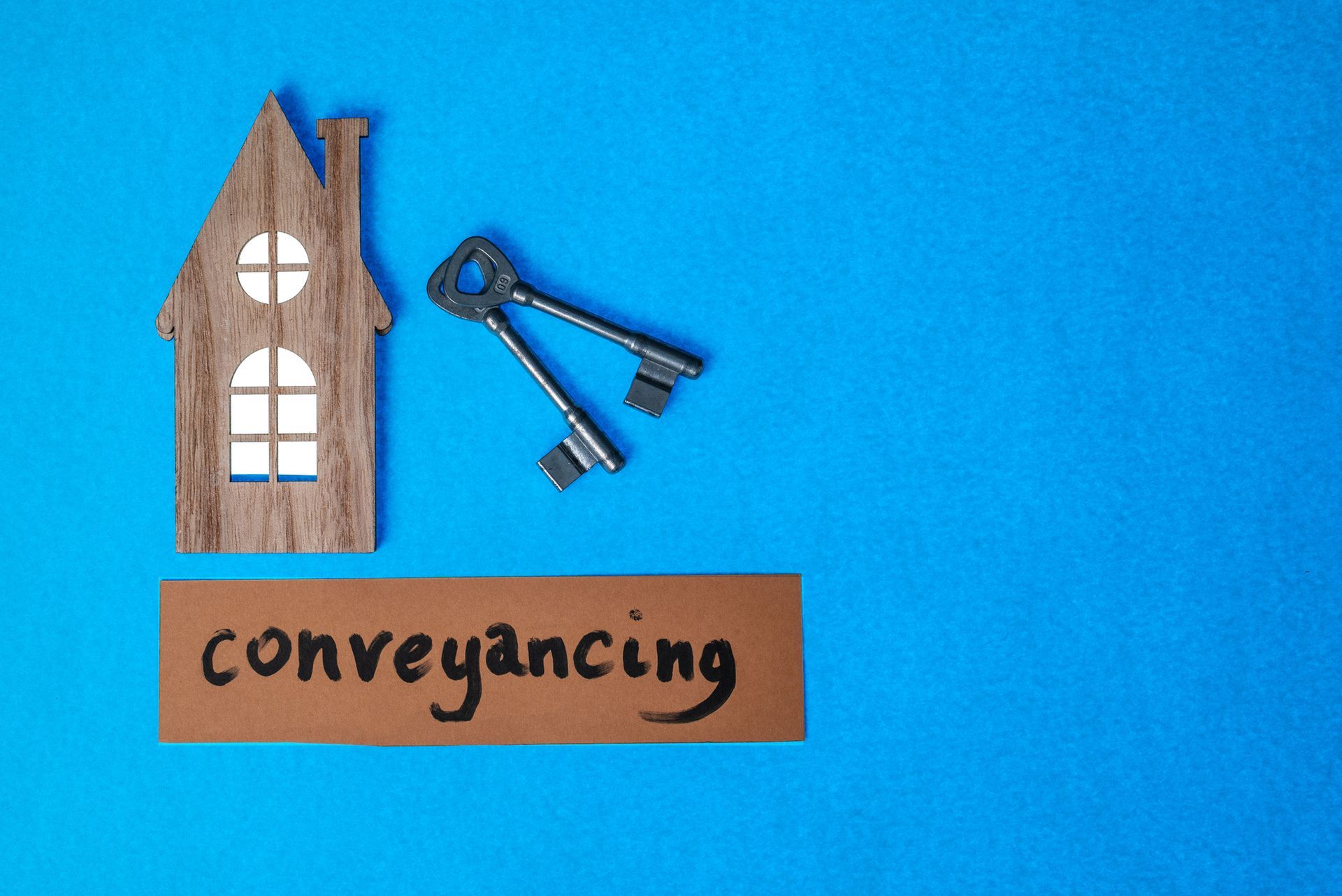 Property conveyancing services concept with a wooden house icon, keys, and text on blue background. Property conveyancing services concept with a wooden house icon, keys, and text on blue background.