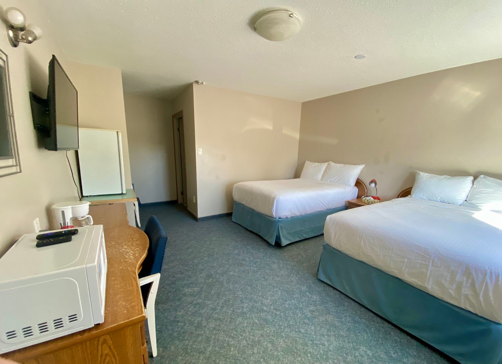 A hotel room with two queen beds, a desk, a microwave, a small refrigerator, and a wall-mounted television.