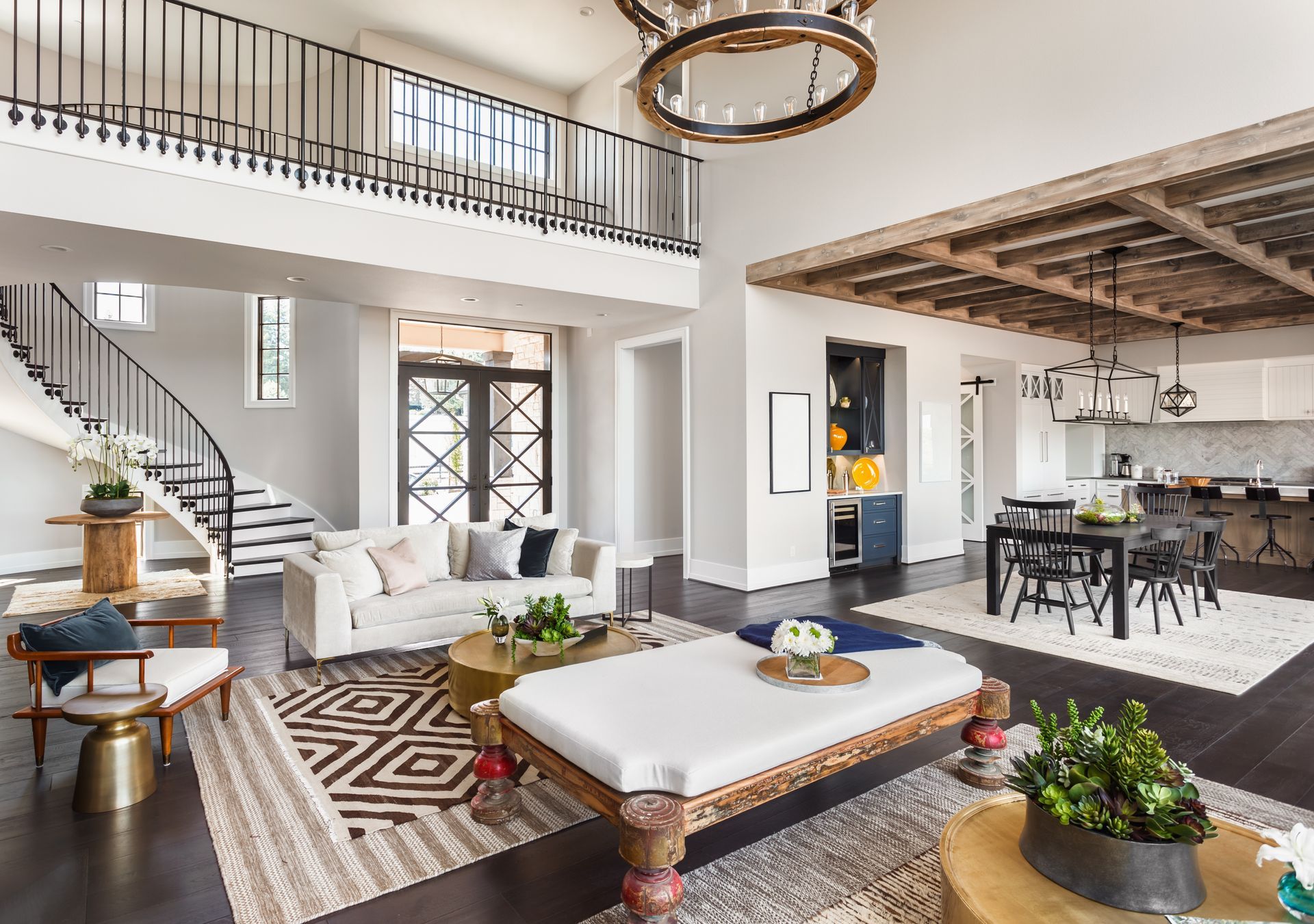 Bright modern living room with staircase, white furniture, patterned rugs, and high ceiling