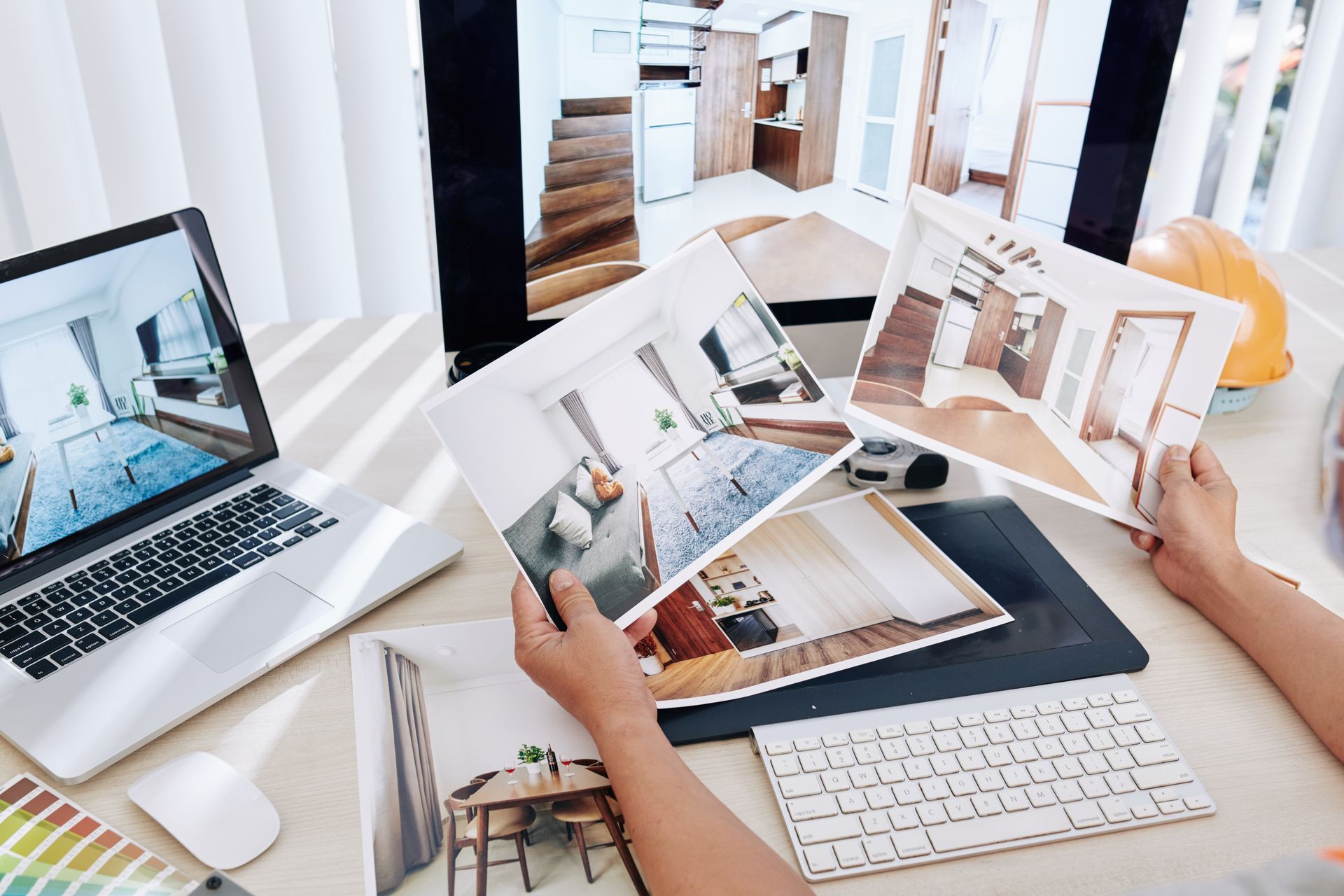 Two people reviewing interior design layouts on laptops and printed photos at a bright desk