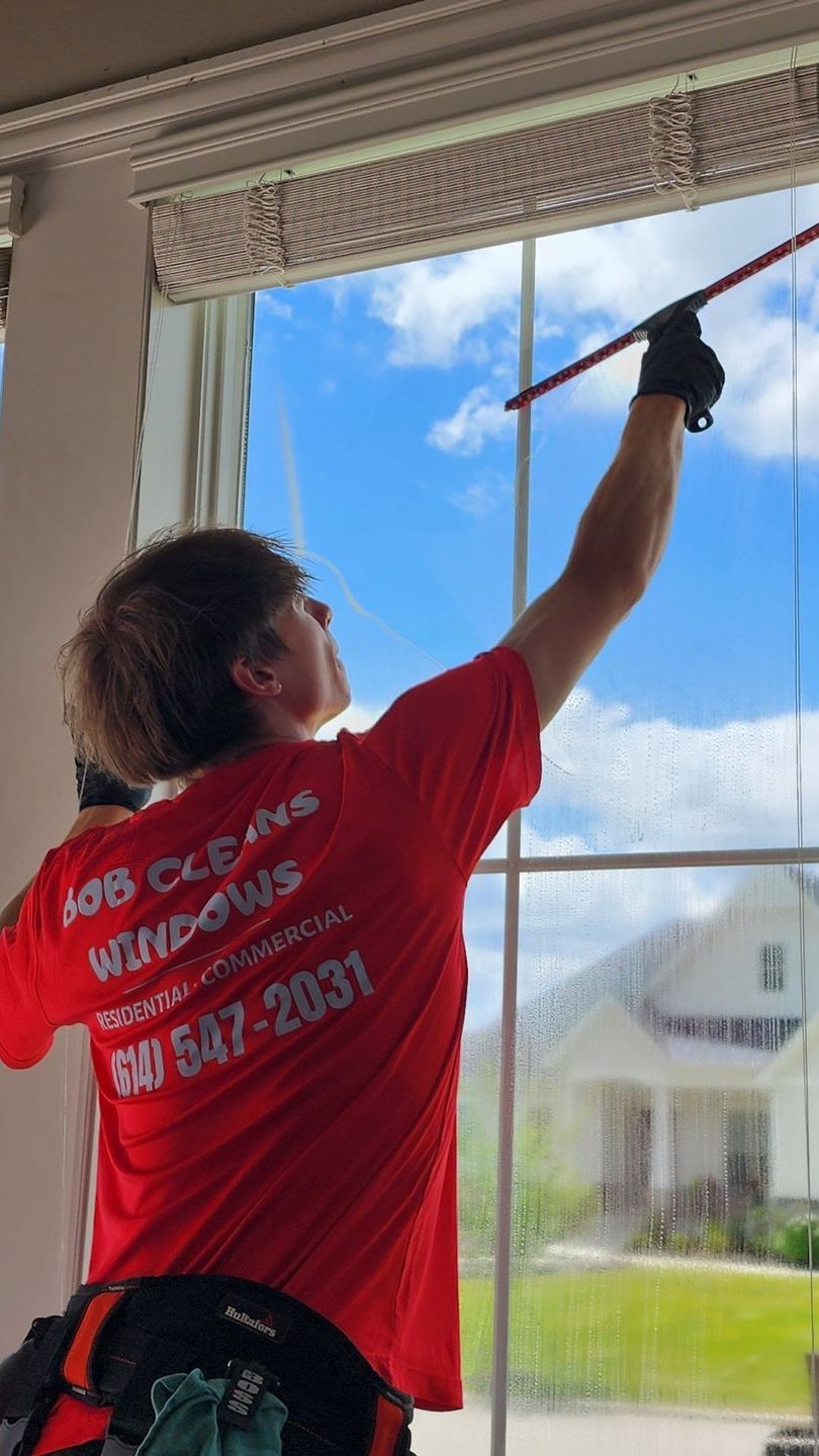 A man in a red shirt is cleaning a window with a squeegee.