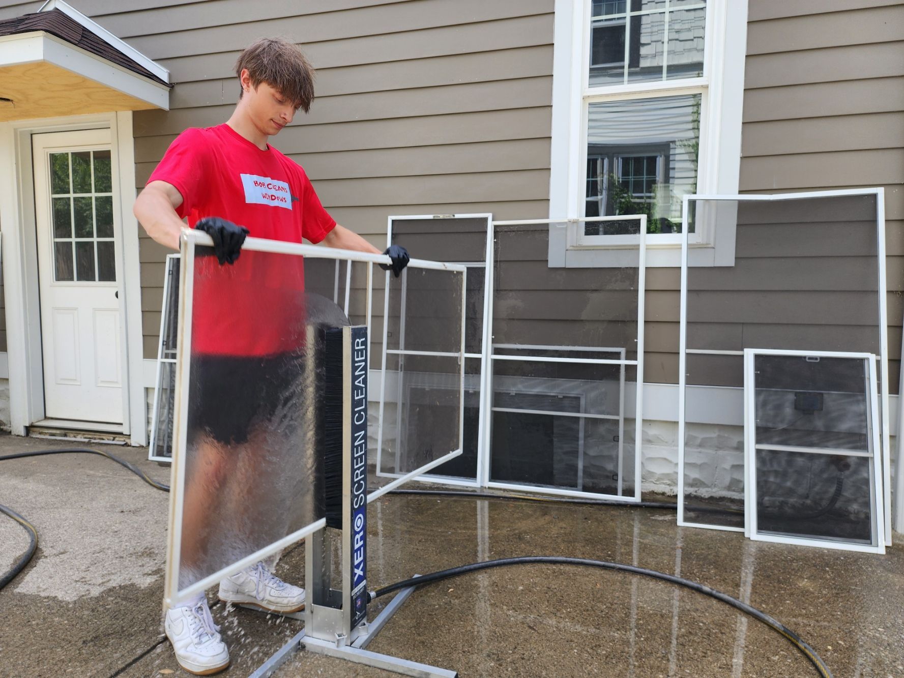 A man in a red shirt is holding a screen door in front of a house.
